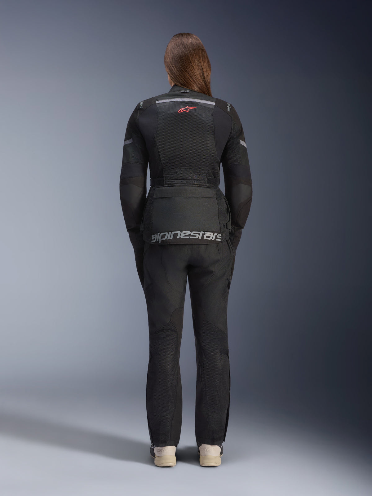 Femme portant la veste Alpinestars Stella Andes Air Drystar® et le pantalon assorti, Noir, vue arrière montrant le grand marquage Alpinestars gris sur la poche du bas du dos, le petit logo étoile rouge en haut du dos, des panneaux de ventilation en maille et des détails réfléchissants pour le touring d'aventure