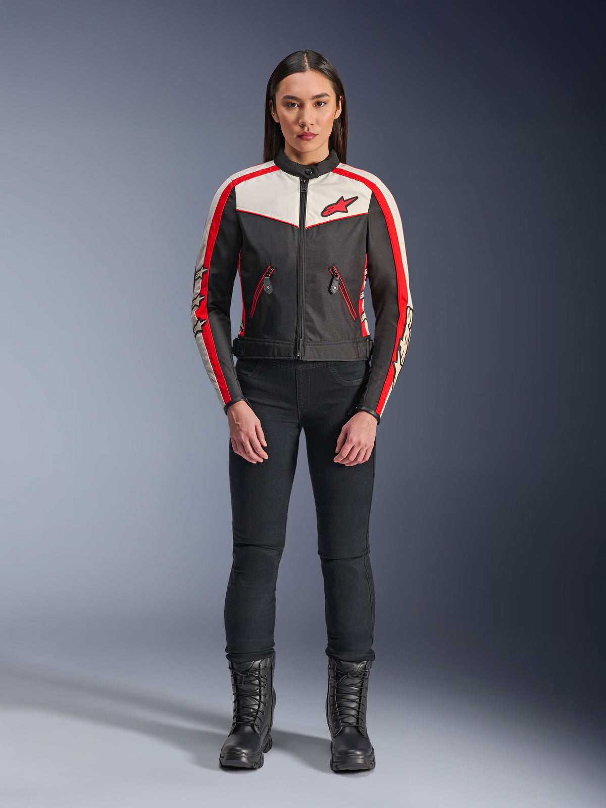 Veste Alpinestars Stella T-Dyno WR, veste de moto textile pour femme, noir, écru et rouge vif, portée par un mannequin avec un pantalon et des bottes noirs, présentant un design d'inspiration vintage avec un logo Alpinestars rouge et des panneaux contrastés.