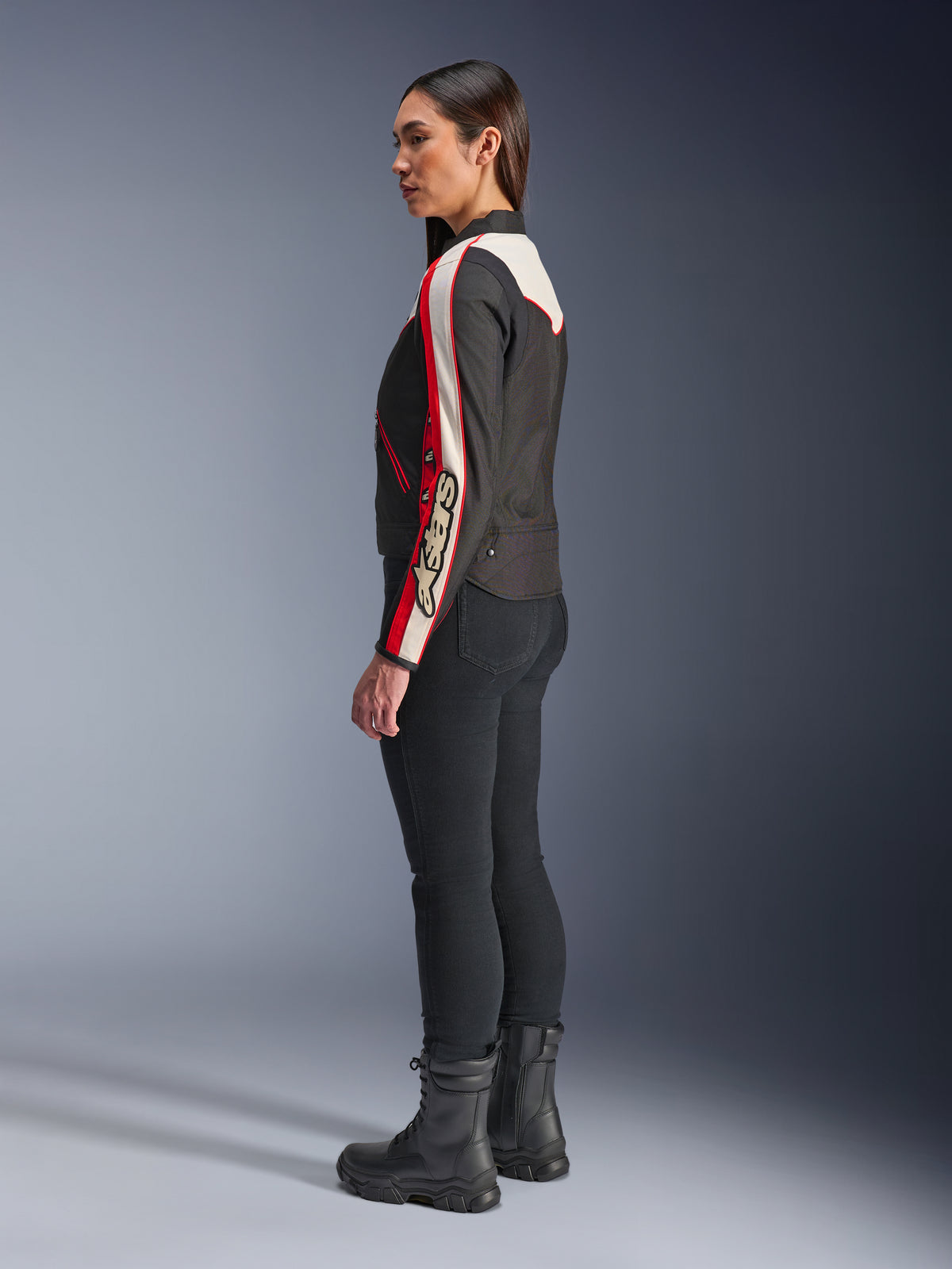 Veste Alpinestars Stella T-Dyno WR, veste de moto en textile pour femme, noir, écru et rouge vif, avec un design d'inspiration vintage et le logo Astars sur la manche, portée avec un pantalon noir ajusté et des bottes noires, coupe biker courte pour la conduite urbaine