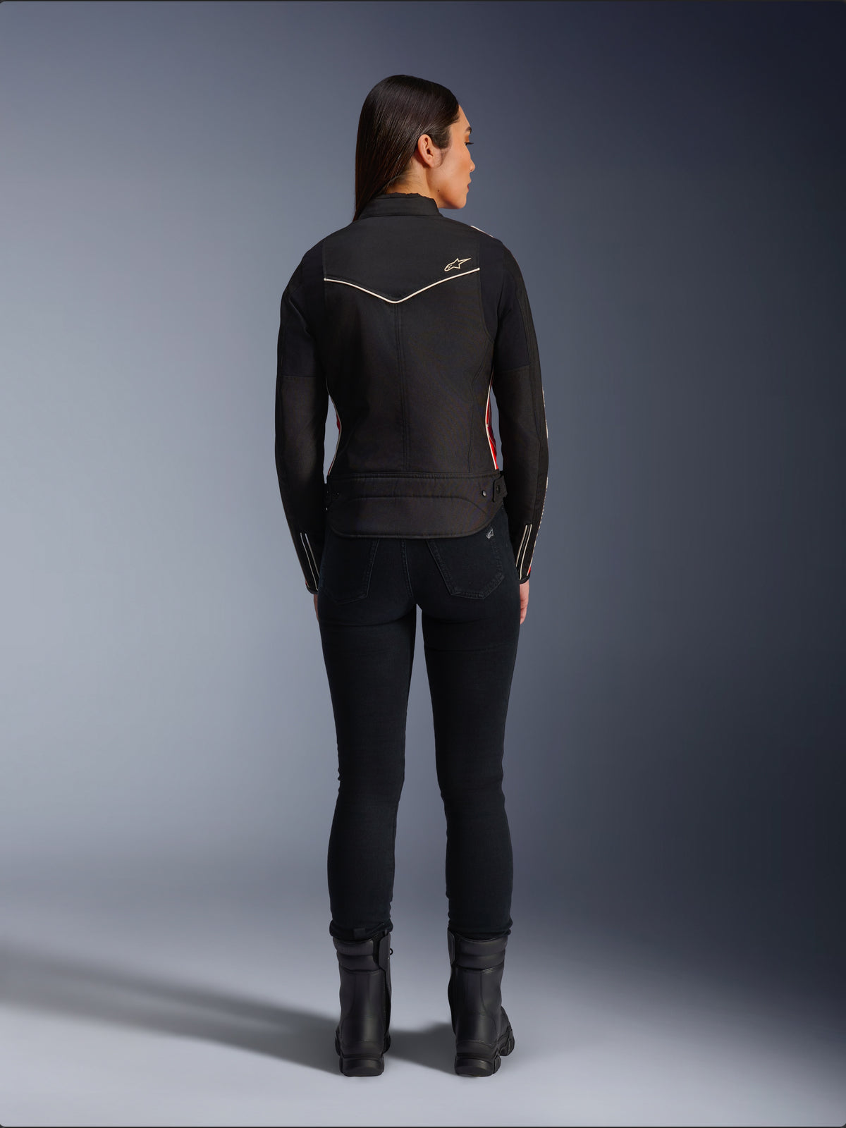 Vrouwelijk model van achteren in de Alpinestars Stella T-Dyno WR Jas in Black Bright Red Fuchsia, textiele motorjas met een kortere biker pasvorm, achteraanzicht met wit sterlogo, gecombineerd met een zwarte broek en zwarte laarzen