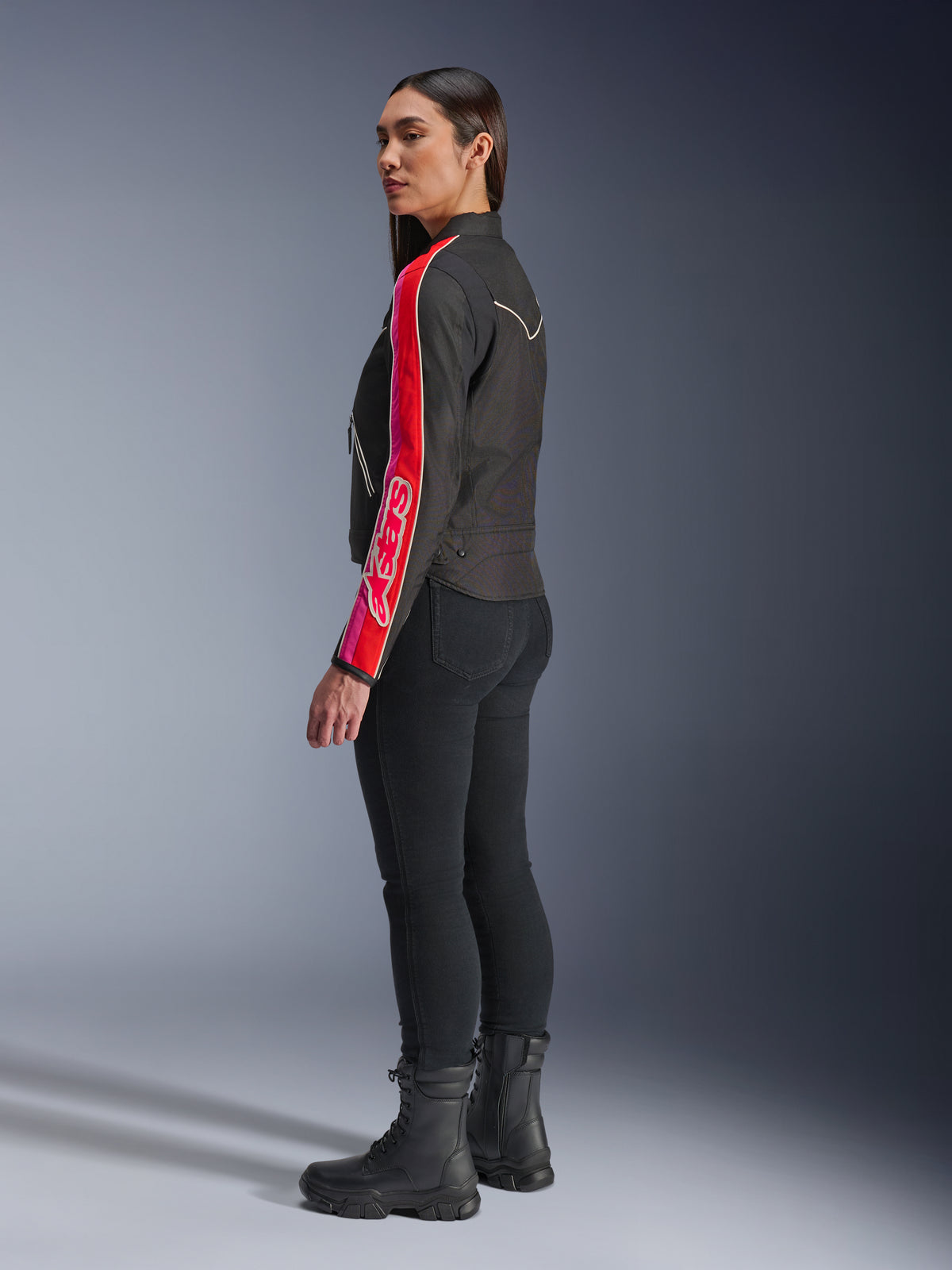 Vrouwelijk model draagt de Alpinestars Stella T-Dyno WR Jas in Black Bright Red Fuchsia, voorzien van opvallende rode en roze strepen met Alpinestars-logo op de mouw, gecombineerd met een zwarte motorbroek en zwarte motorlaarzen in een studio-omgeving.