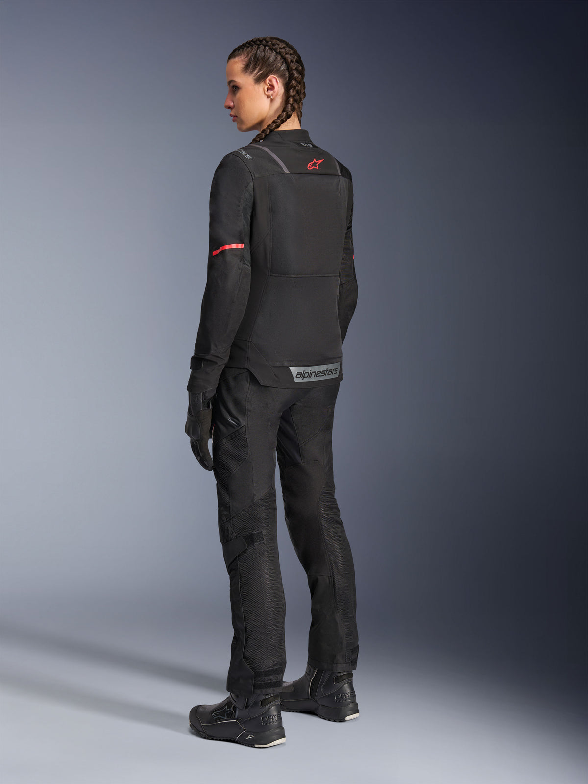 Alpinestars Stella ST-2 Air Jacke, Damen-Motorradjacke, Schwarz mit roten Akzenten an den Ärmeln und am oberen Rücken, Rückansicht am Modell mit passender schwarzer Motorradhose und Stiefeln, reflektierendes Alpinestars-Branding, moderne Textilkonstruktion