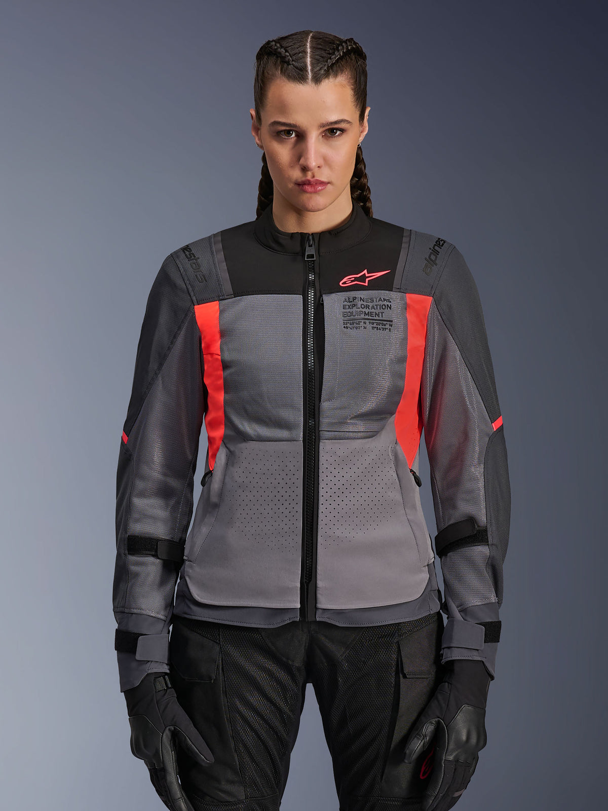 Alpinestars Stella ST-2 Air motorjas, dames motorjas, donkergrijs en koraalrood, model draagt geventileerde textiele jas met mesh-panelen, felle koraalrode accenten en logo op de borst, moderne adventure rijstijl