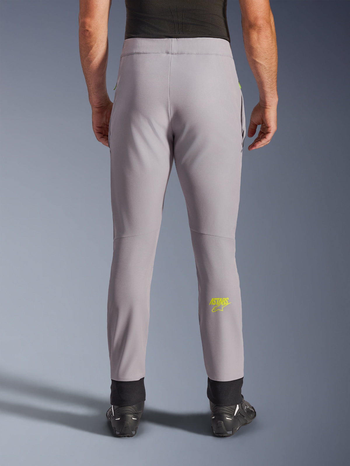 Alpinestars Aeroshell broek, motorbroek, Mid Gray en Yellow Fluo, achteraanzicht met geel Astars-logo op de kuit, zwarte elastische enkelmanchetten, modern softshell textielontwerp voor ritten op de weg en casual gebruik