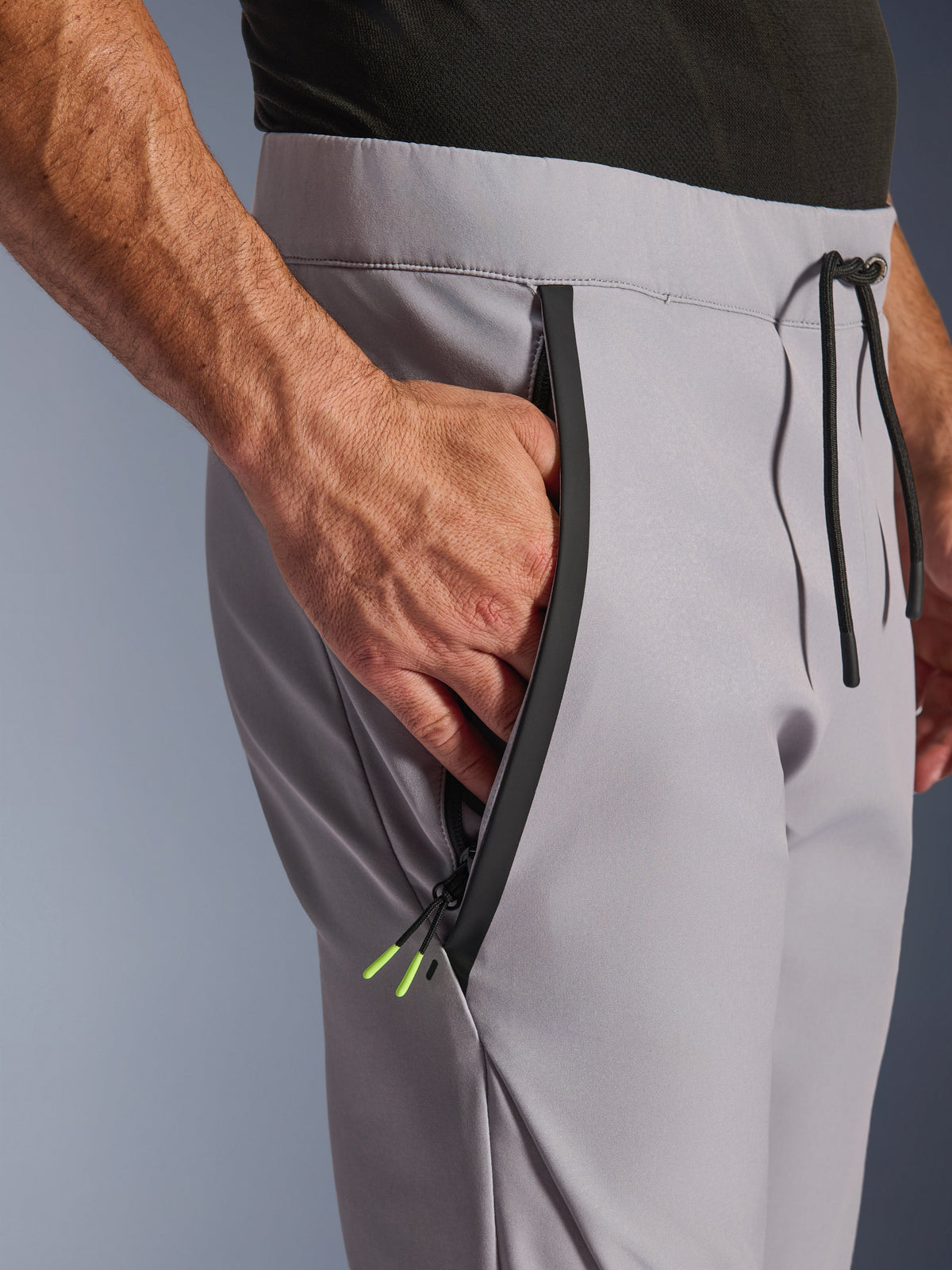 Alpinestars Aeroshell-broek, Mid Gray Yellow Fluo, close-up van de voorzak met rits en taille, zwarte getapete rits met fluorgele uiteinden, elastische tailleband met zwart trekkoord, crossover sportieve softshell motorbroek