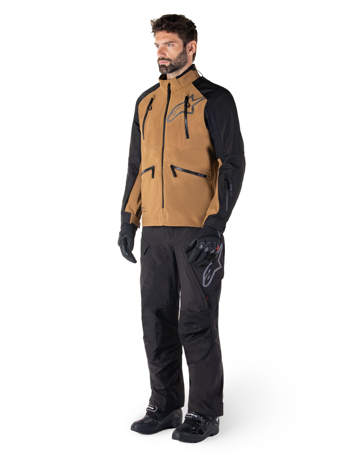 Alpinestars Hyde XT Drystar® broek, adventure motorbroek, zwart, gedragen met een bruine en zwarte technische jas, zwarte handschoenen en laarzen, met een over-de-laars ontwerp voor off-road en dual-sport rijden