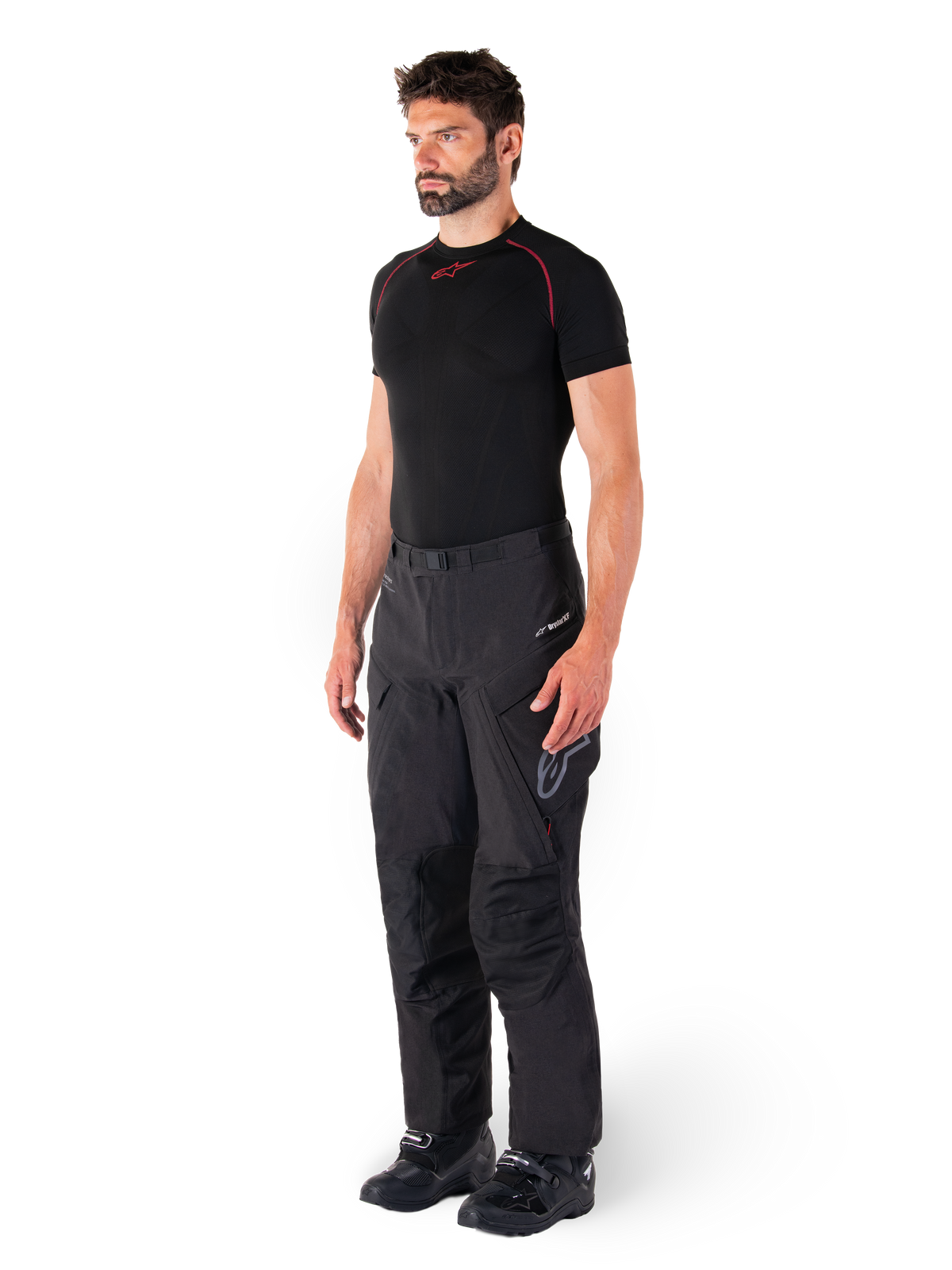 Alpinestars Hyde XT Drystar® broek, zwarte adventure touring motorbroek gedragen door een model met een zwart compressieshirt en zwarte laarzen, voorzien van een technische waterdichte constructie en Drystar®XF-branding.