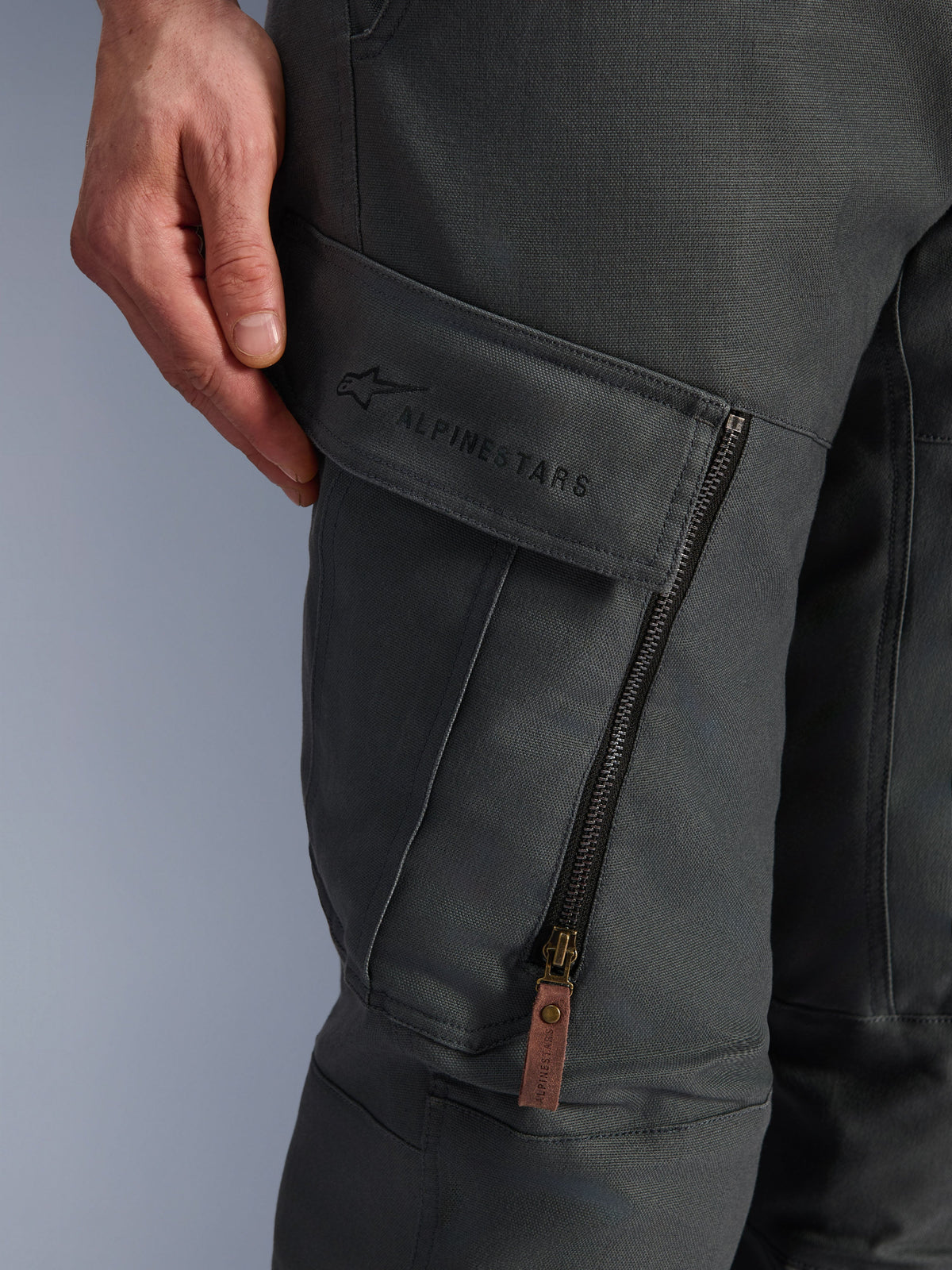 Pantalon Alpinestars Borrego Drystar®, gris anthracite, gros plan sur la poche cargo de la cuisse avec logo brodé, matière en toile cirée texturée, fermeture éclair de ventilation verticale avec tirette en cuir marron