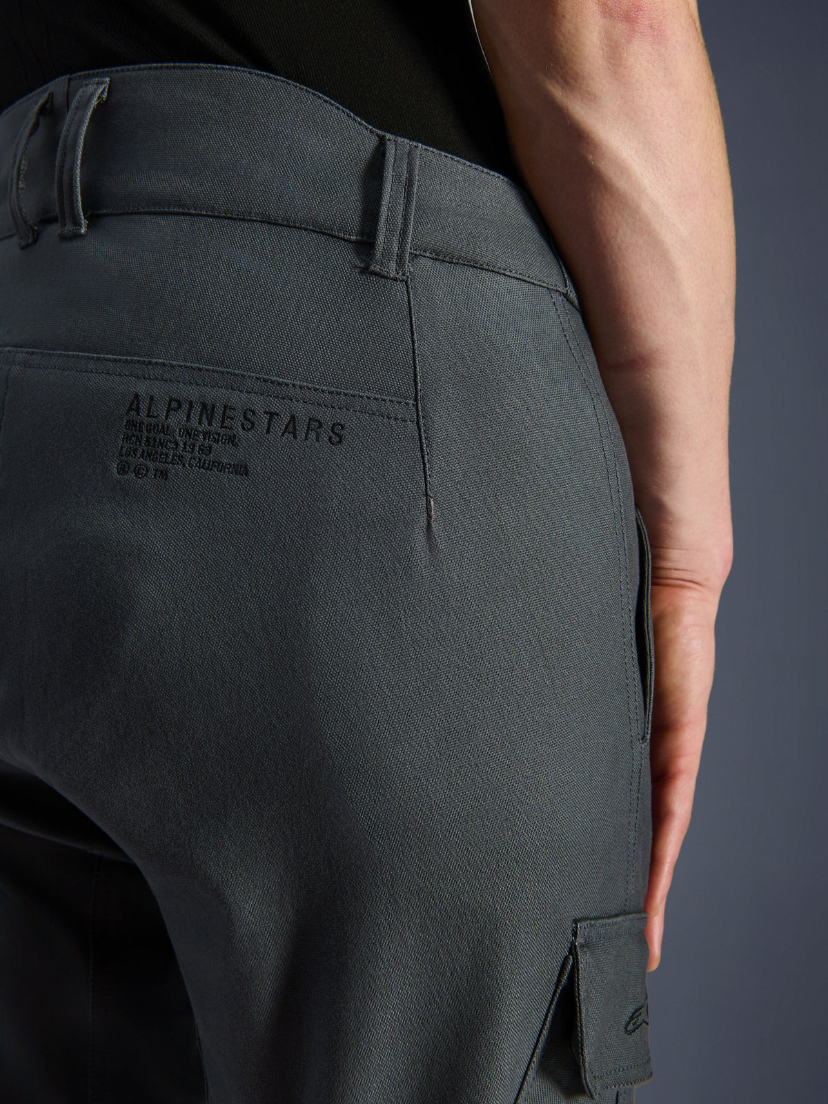 Pantalon Alpinestars Borrego Drystar®, pantalon de moto, gris anthracite, gros plan de la zone arrière de la hanche présentant le marquage et le slogan Alpinestars, textile durable avec un aspect toile cirée, vêtement d'aventure