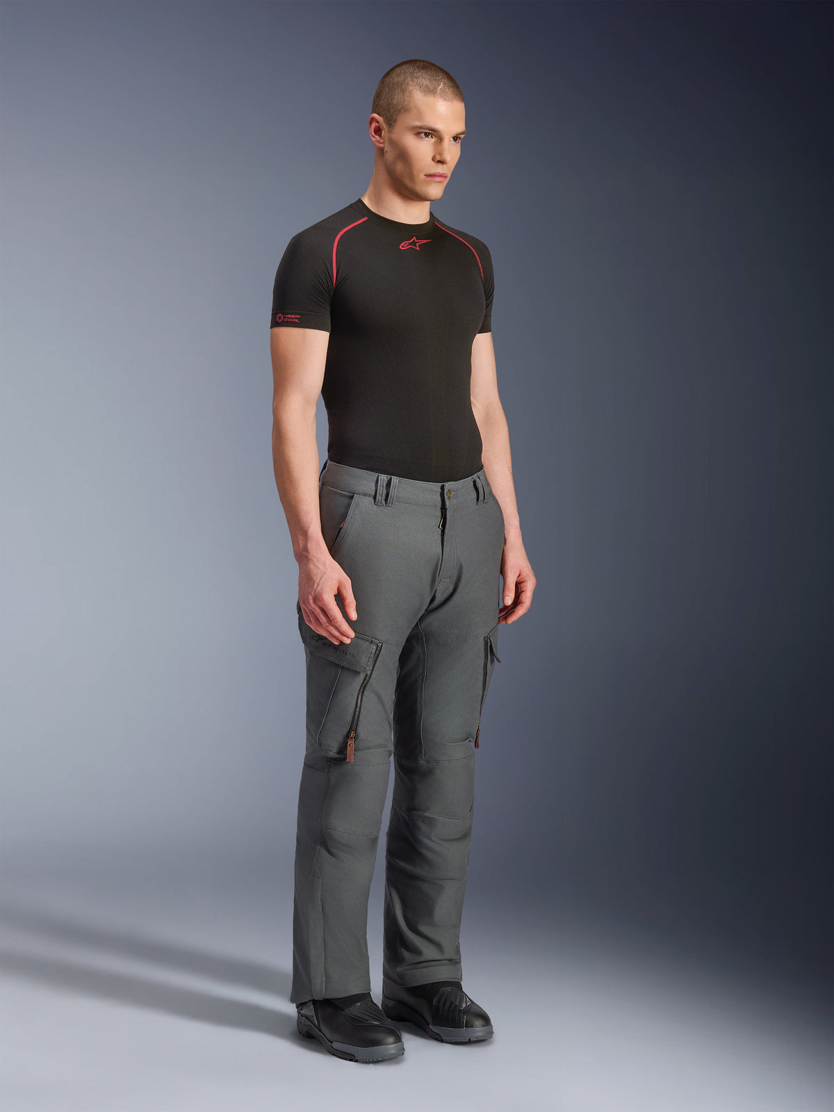 Mannequin homme portant le pantalon Alpinestars Borrego Drystar®, pantalon de moto d'aventure gris anthracite, design inspiré des vêtements de travail avec poches cargo et ventilations zippées, associé à une couche de base noire à manches courtes et des bottes noires.