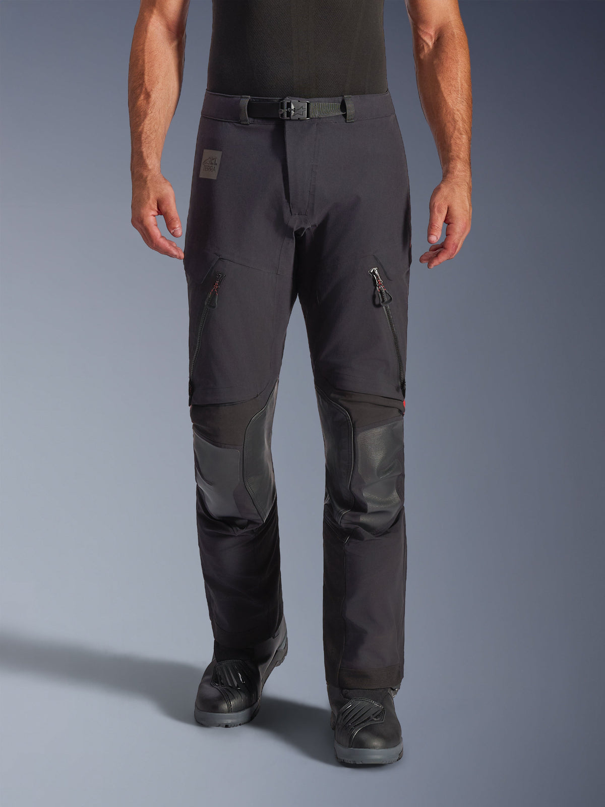 Alpinestars Halo Pro Drystar® XF Laminierte Hose in Black Dark Shadow, Adventure-Motorradhose, Vorderansicht am Model mit magnetischer Taillenschnalle, Belüftungsreißverschlüssen an den Oberschenkeln und verstärkten Leder-Knieeinsätzen, kombiniert mit schwarzen Motorradstiefeln