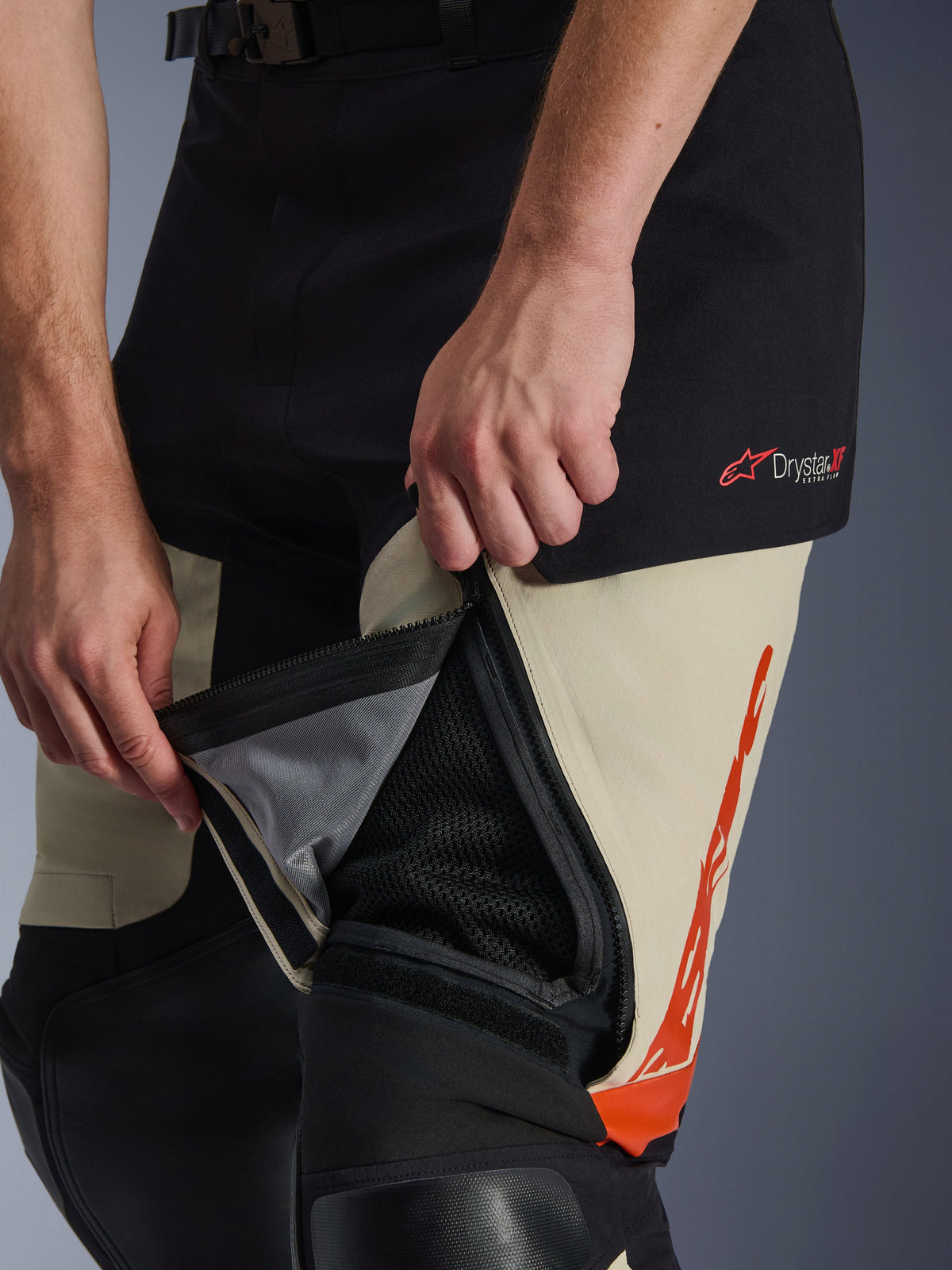 Alpinestars Halo Pro Drystar® XF Laminierte Hose, Mastic Black, Nahaufnahme der geöffneten Oberschenkel-Belüftungsöffnung mit Mesh-Einsatz für Luftzirkulation, rotes Drystar XF Logo und orangefarbene Grafikelemente