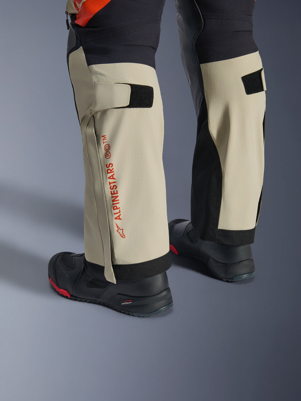Alpinestars Halo Pro Drystar® XF Laminierte Hose, Mastic Black, Nahaufnahme der Unterschenkel mit rotem Alpinestars-Branding und Klettverschluss-Wadenverstellern, getragen mit schwarzen Adventure-Stiefeln