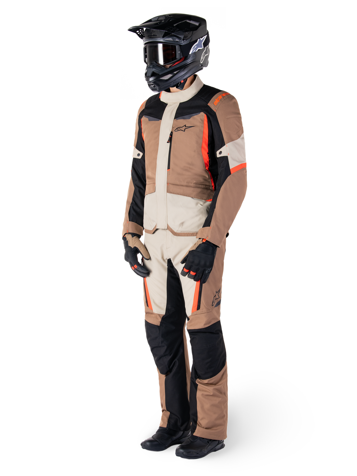Rider wearing Alpinestars ST-1 Waterproof adventure touring suit, Dark Khaki Sand and Black jacket and pants with Red Fluo accents, black helmet and gloves, showcasing a complete waterproof outfit for all-weather motorcycle riding