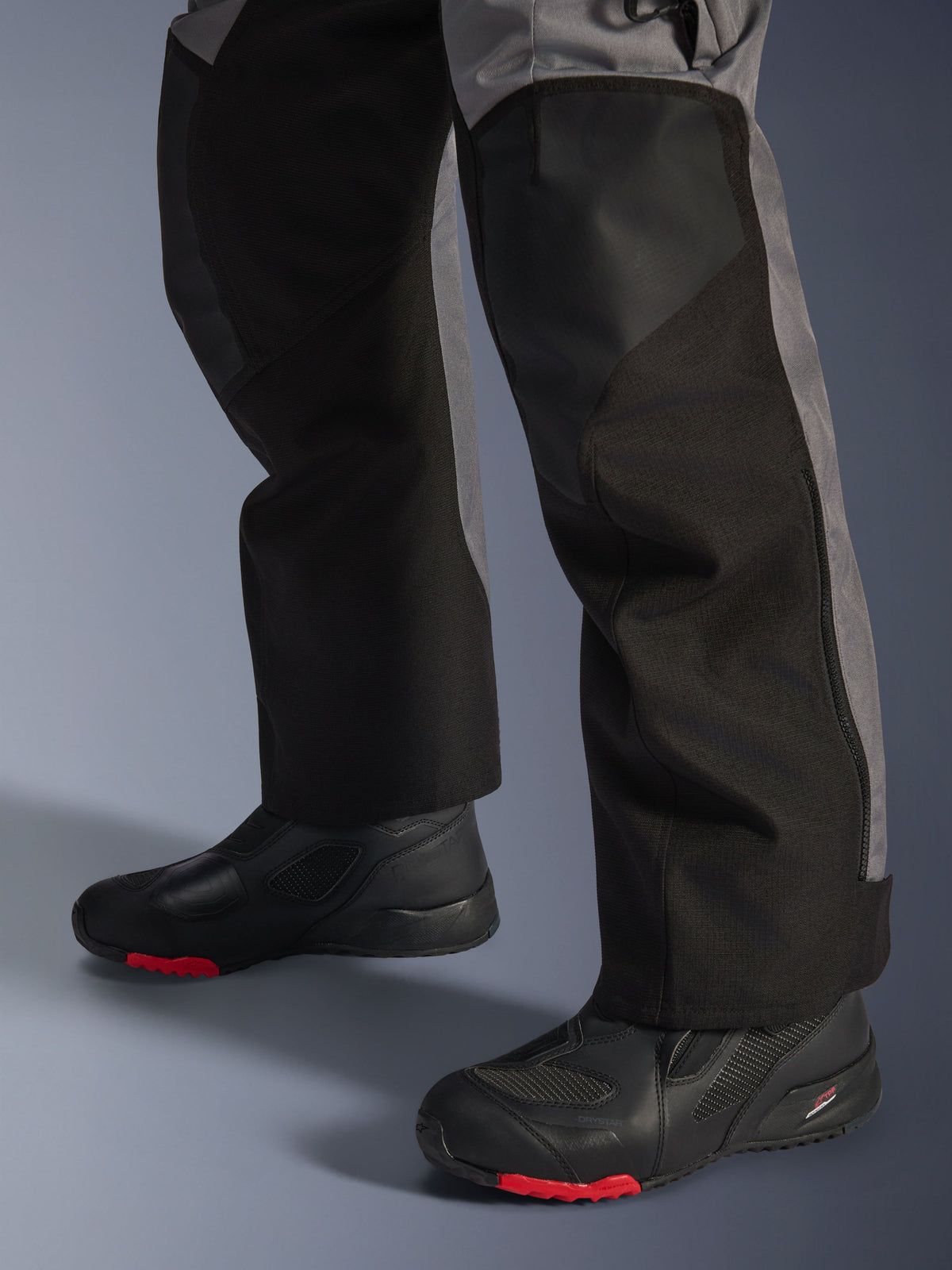 Alpinestars Andes V4 Drystar® broek, textiele motorbroek, zwart en donkergrijs, gedragen met zwarte motorlaarzen met rode zolen, adventure touring ontwerp met verstevigde beenpanelen en een rechte pasvorm.