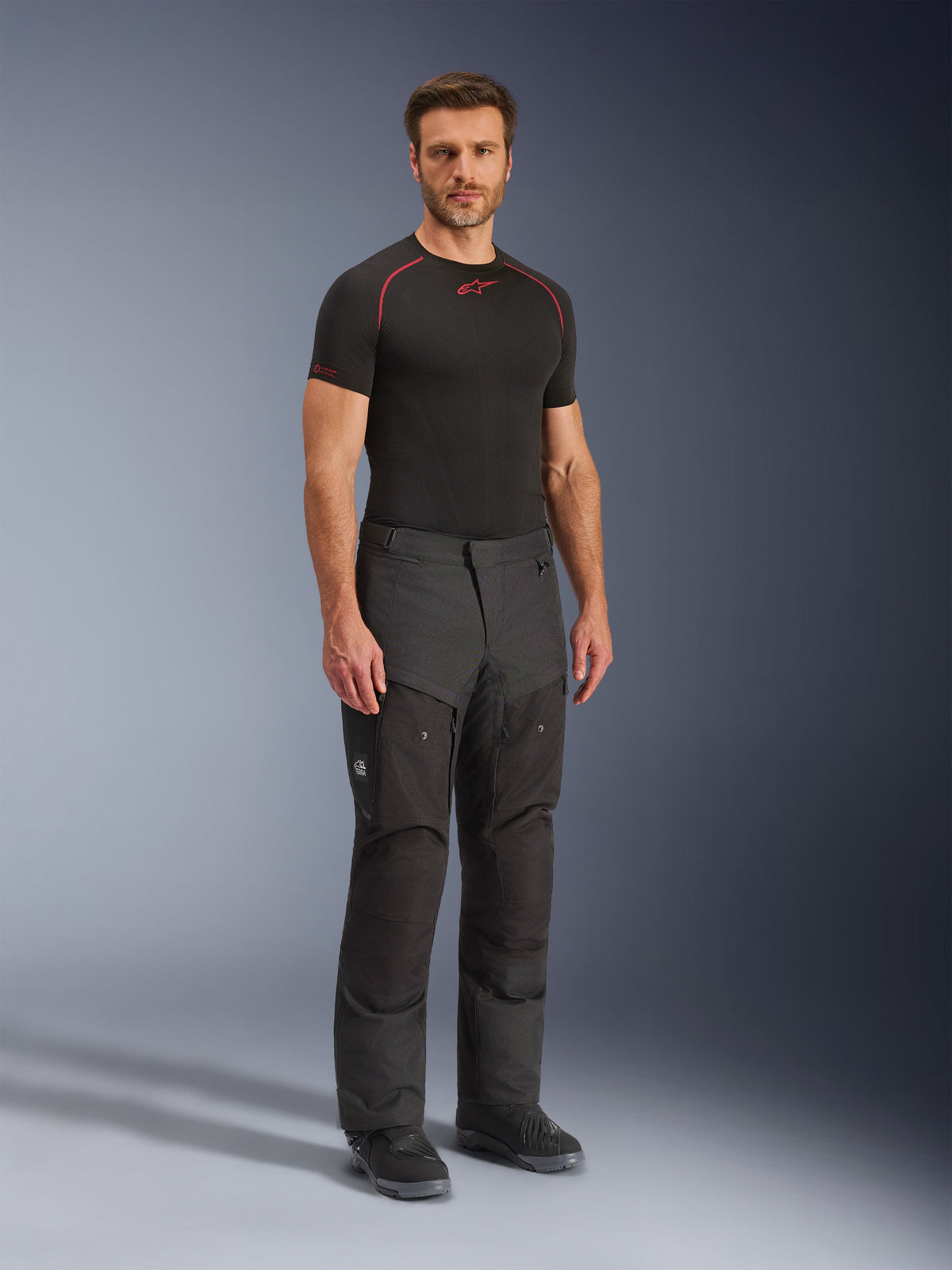 Alpinestars Cusco Drystar® Hose, schwarze Motorrad-Textilhose, getragen von einem Model mit schwarzem Base Layer und Stiefeln, Ripstop-Gewebe, große Cargotaschen mit „Terra“-Branding, ergonomisches Design für Adventure-Riding