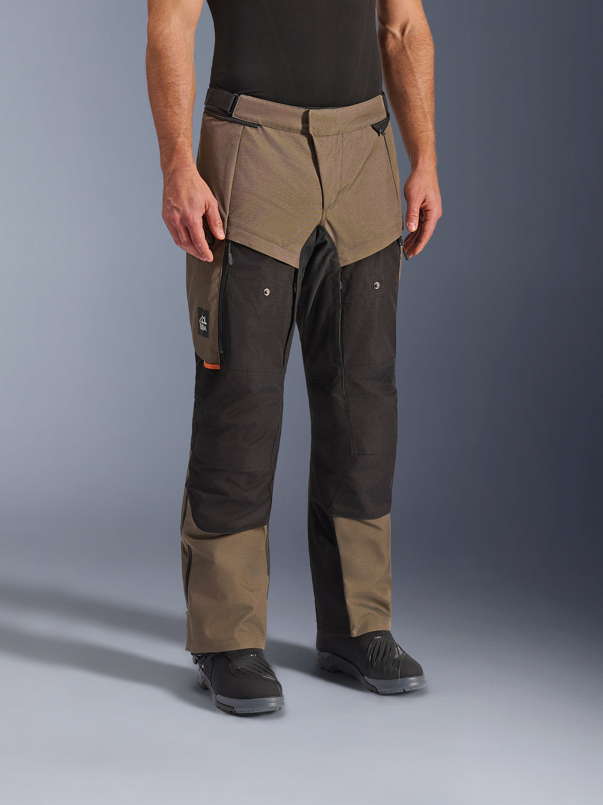 Pantalon Alpinestars Cusco Drystar®, pantalon de moto adventure, Walnut Black, présenté sur un mannequin avec des bottes noires, doté d'un design multi-panneaux marron et noir avec des poches zippées et des genoux renforcés pour le touring
