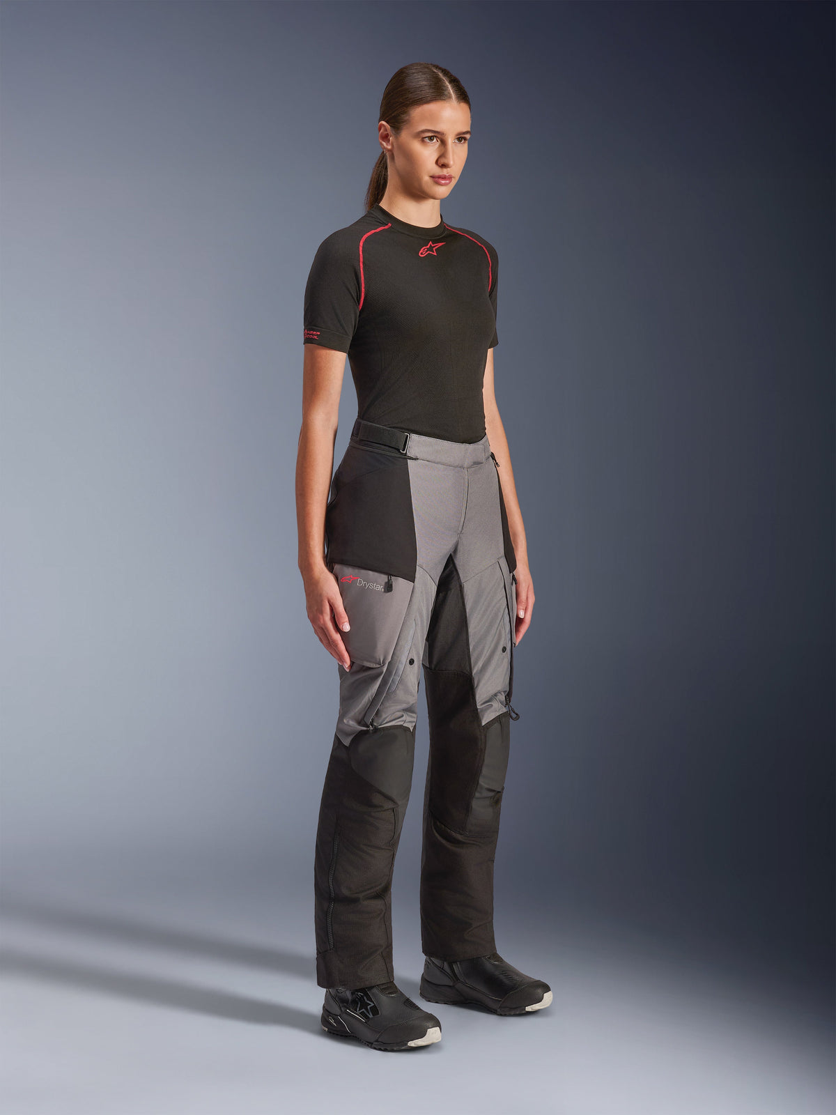 Pantalon Alpinestars Stella Andes V4 Drystar®, pantalon de moto adventure pour femme, noir et gris foncé, porté par un mannequin avec une sous-couche Alpinestars noire et des bottes noires, doté de panneaux renforcés, d'un logo Drystar rouge et de poches cargo.