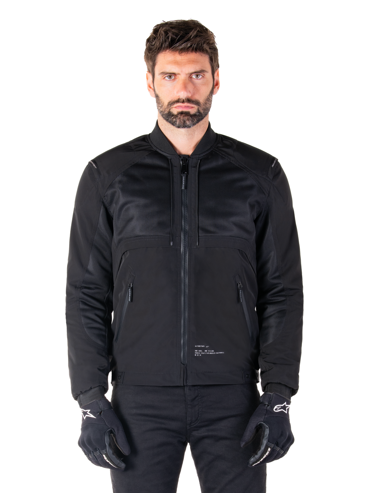 Alpinestars Mootant Wasserdichter Parka, schwarze Motorradjacke, Vorderansicht an männlichem Model, mit modularer Textilkonstruktion, Mesh-Einsätzen zur Belüftung, geripptem Kragen und Reißverschlusstaschen, getragen mit schwarzen Handschuhen mit weißem Alpinestars-Branding