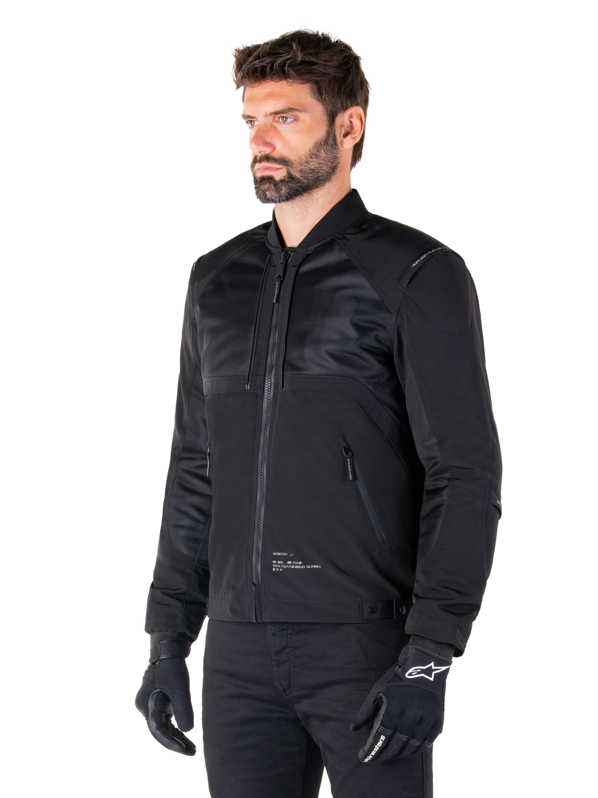 Alpinestars Mootant Waterproof Parka, modulare schwarze Motorradjacke in der Bomber-Konfiguration mit Mesh-Einsätzen am Oberkörper und geripptem Kragen, getragen von einem Modell mit schwarzen Motorradhandschuhen und Hosen, urbaner zeitgenössischer Streetwear-Stil.