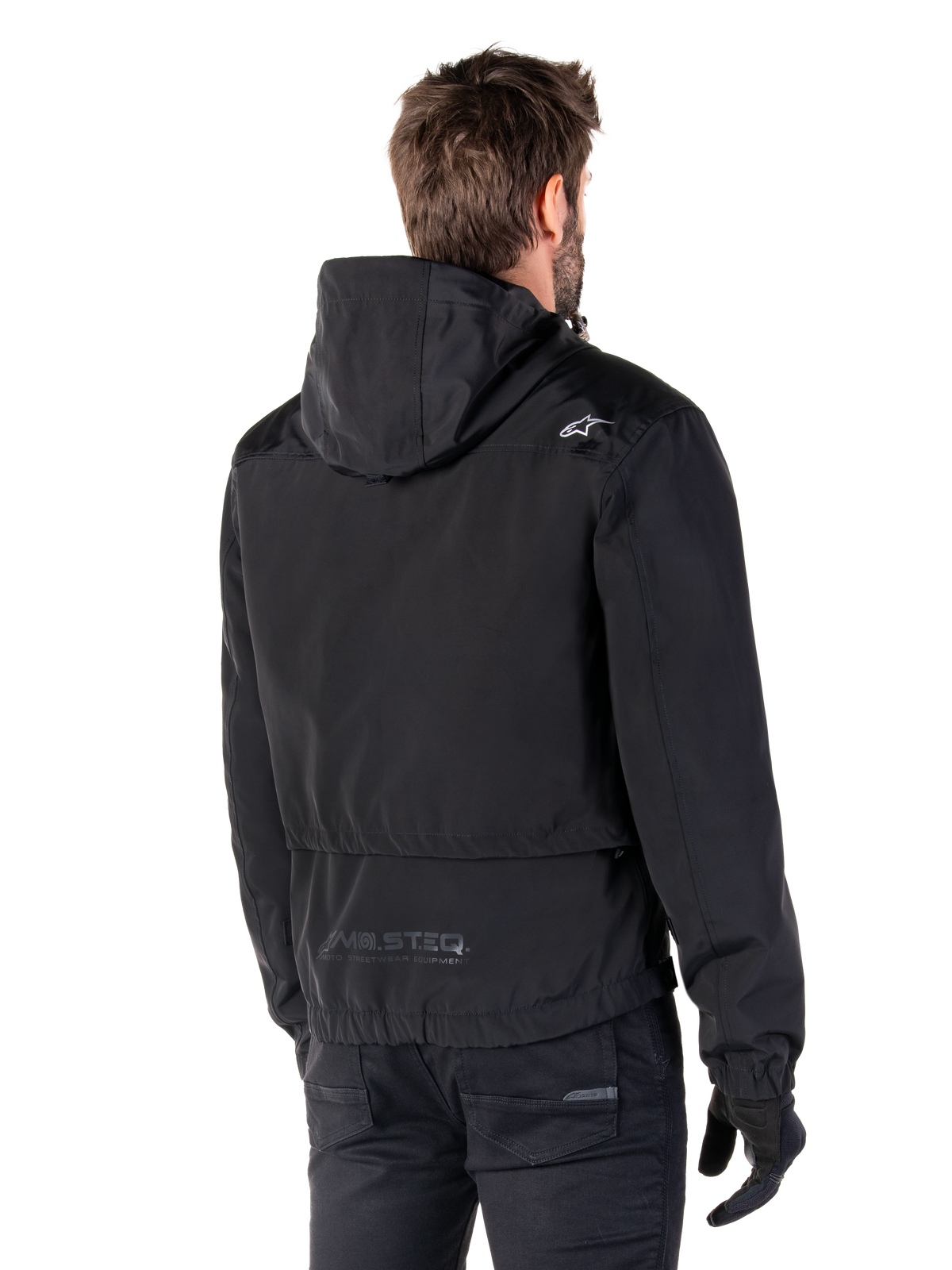 Alpinestars Mootant Wasserdichter Parka, schwarze Motorradjacke, Rückansicht mit Kapuzendesign, weißes Logo auf der Schulter und reflektierendes MO.ST.EQ. Branding am unteren Rücken, urbane zeitgemäße Fahrausrüstung