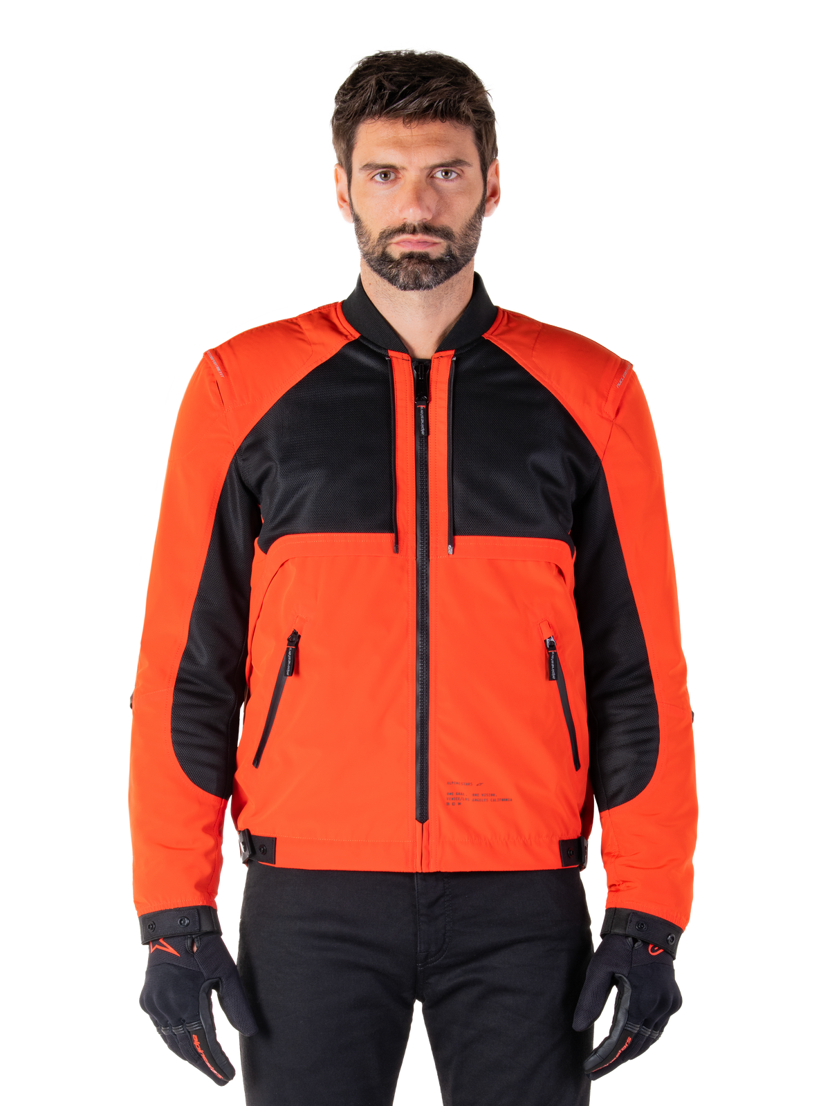 Alpinestars Mootant Waterproof Parka in Spicy Orange en zwart, modulaire motorjas getoond in een bomberjack-configuratie op een mannelijk model, met zwarte mesh panelen op de bovenborst, feloranje torso en mouwen, ritssluiting aan de voorzijde en een geribbelde kraag, gecombineerd met zwarte handschoenen en broek