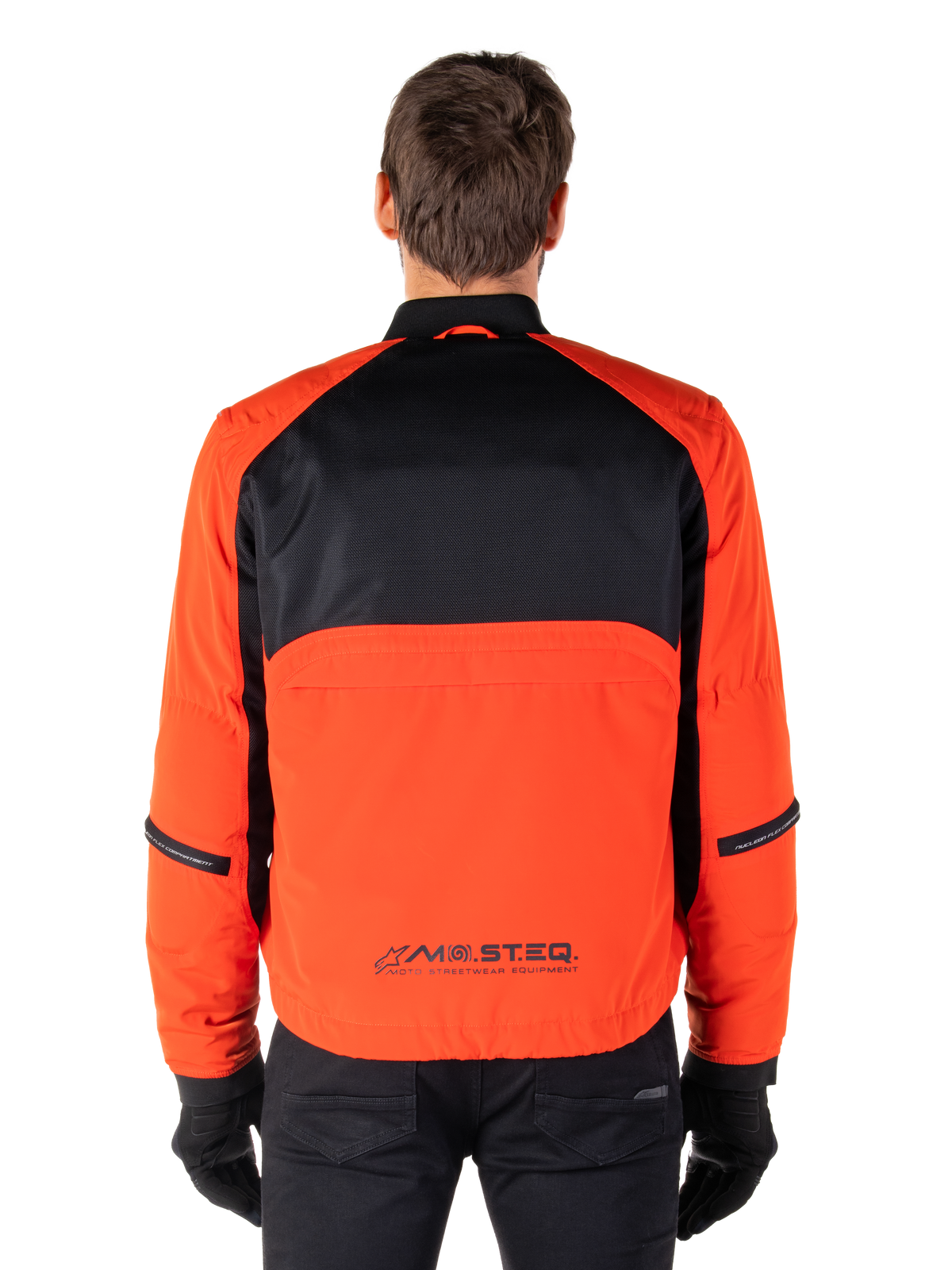 Alpinestars Mootant Waterproof Parka, motorjas, Spicy Orange en zwart, achteraanzicht, met zwart mesh op de bovenrug en een oranje onderpaneel met MO.ST.EQ.-logo, gedragen met een zwarte broek en handschoenen.