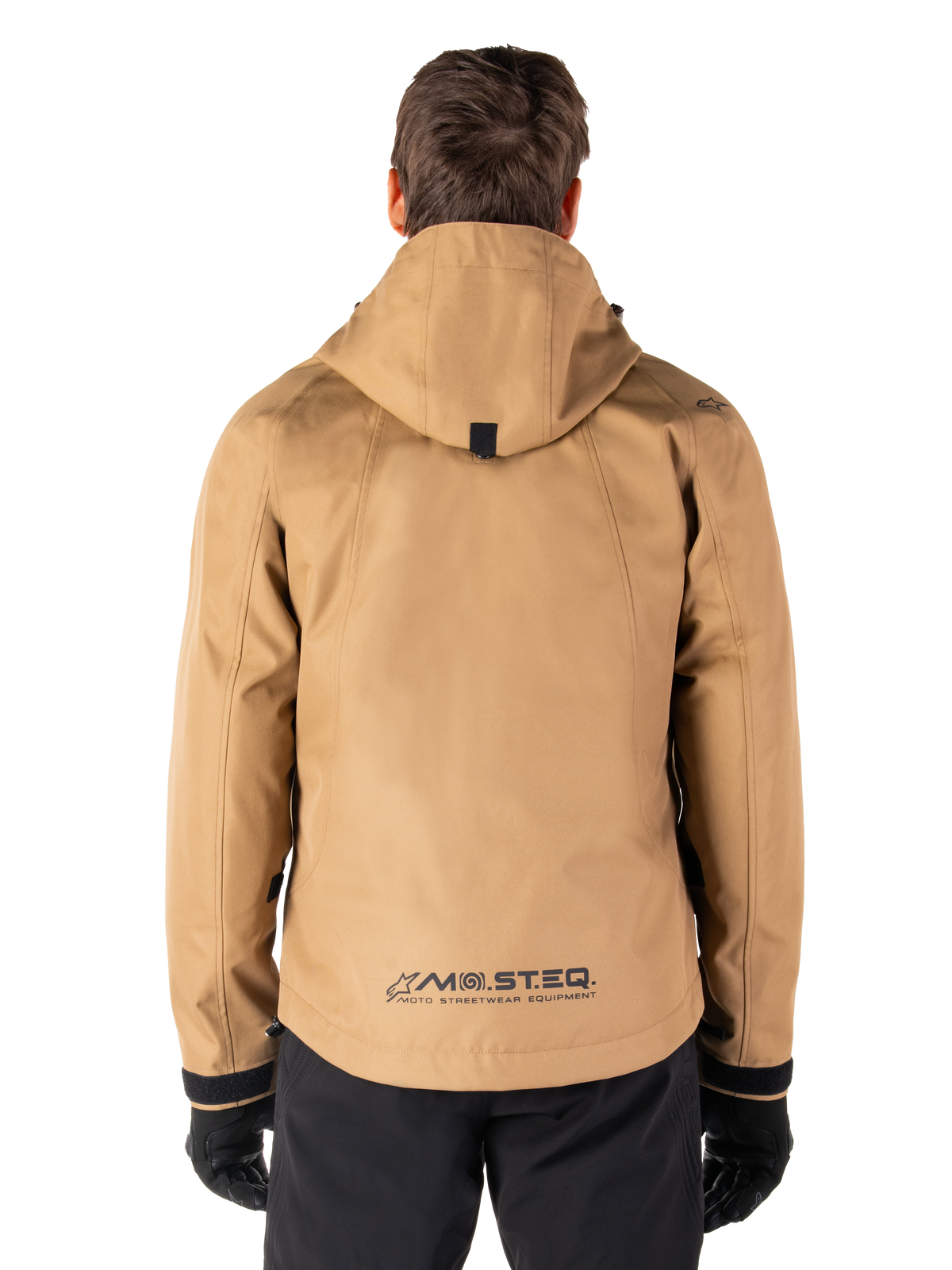 Alpinestars Morush Wasserdichter Parka, Utility Brown, Rückansicht, mit Kapuze und MO.ST.EQ.-Branding am unteren Rücken, kombiniert mit schwarzer Hose und Handschuhen, moderne von Streetwear inspirierte Motorradbekleidung