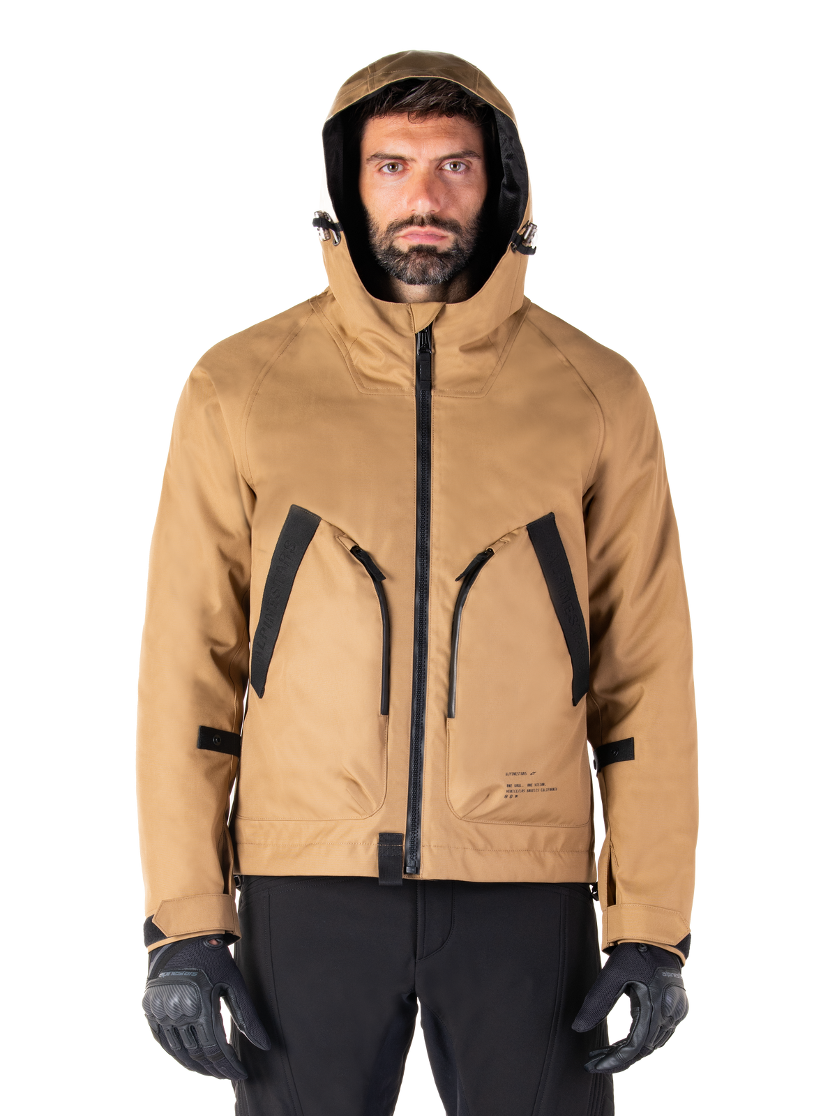 Alpinestars Morush Wasserdichter Parka, Motorradjacke, Utility Brown, Kapuzendesign im Streetwear-Stil mit großen, schwarz akzentuierten Fronttaschen, kombiniert mit schwarzen Fahrhandschuhen und Hosen, moderne urbane Motorradausrüstung