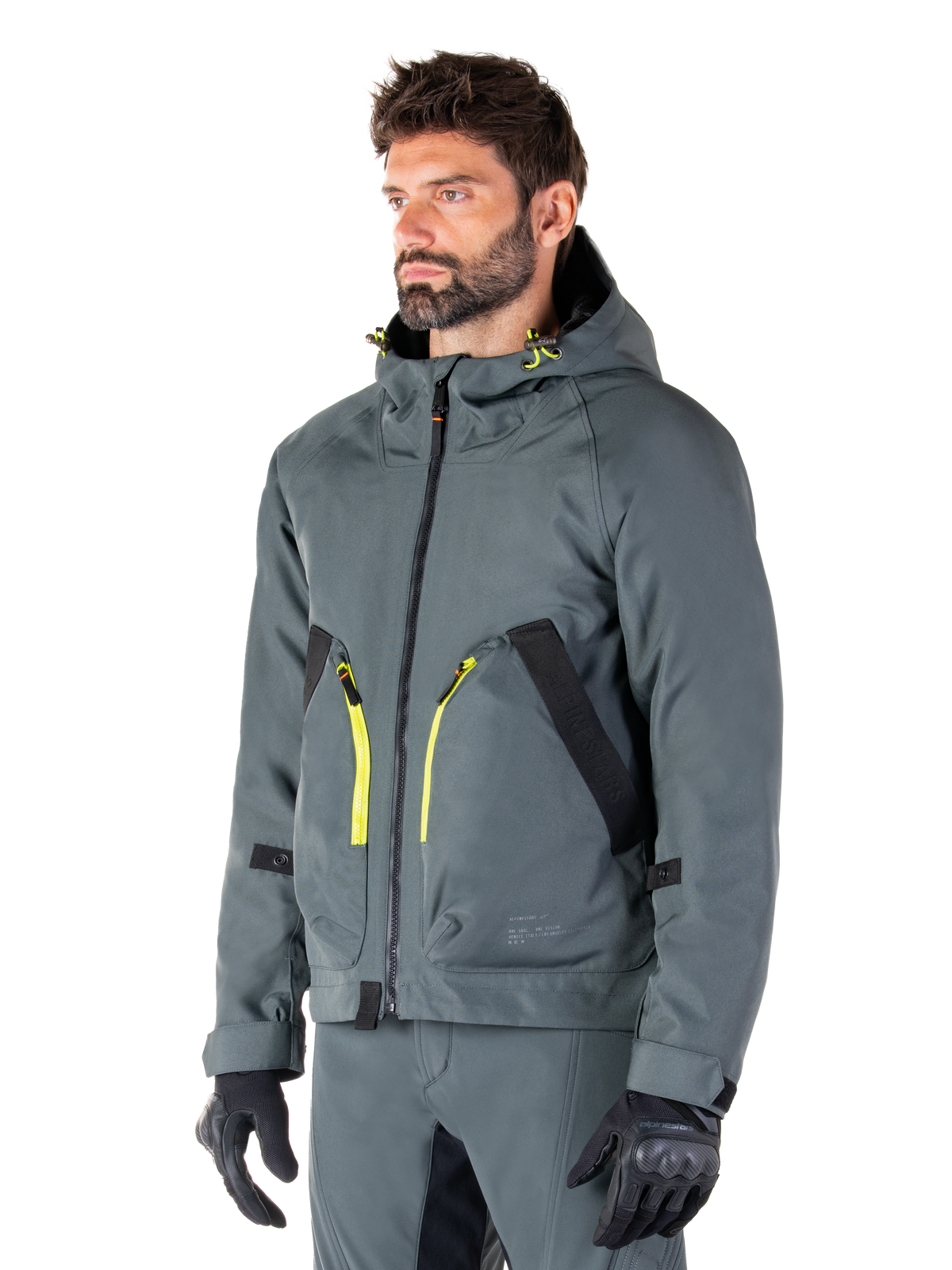 Alpinestars Morush Wasserdichter Parka, Motorradjacke in Urban Gray, Design mit Kapuze und leuchtend gelben Reißverschluss-Akzenten, schwarze Taschendetails, kombiniert mit passender grauer Motorradhose und schwarzen Handschuhen, moderne, von Streetwear inspirierte Motorradbekleidung.
