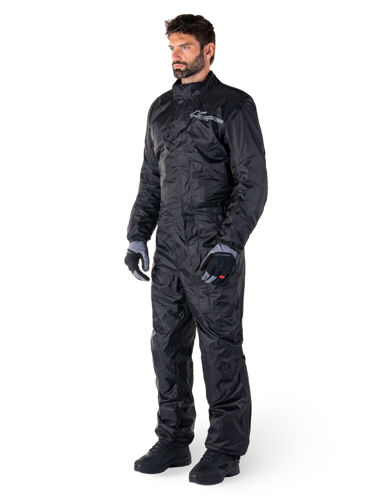 Alpinestars Hurricane Rain V2 Suit, Black, one-piece waterproof motorcycle rain suit, worn with gloves and boots, featuring reflective Alpinestars branding on the chest, lightweight design for wet weather protection