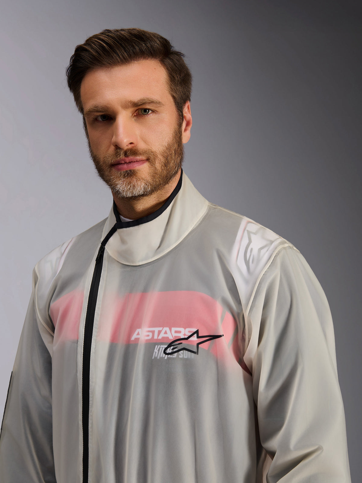 Alpinestars Kart Regenanzug, Karting-Regenüberkombi, Transparent, von einem Mann getragen, durchsichtiges wasserdichtes Material mit sichtbaren rot-weißen Details des darunterliegenden Rennanzugs, hoher Kragen mit schwarzem Reißverschluss und Alpinestars Stern-Logo auf der Brust