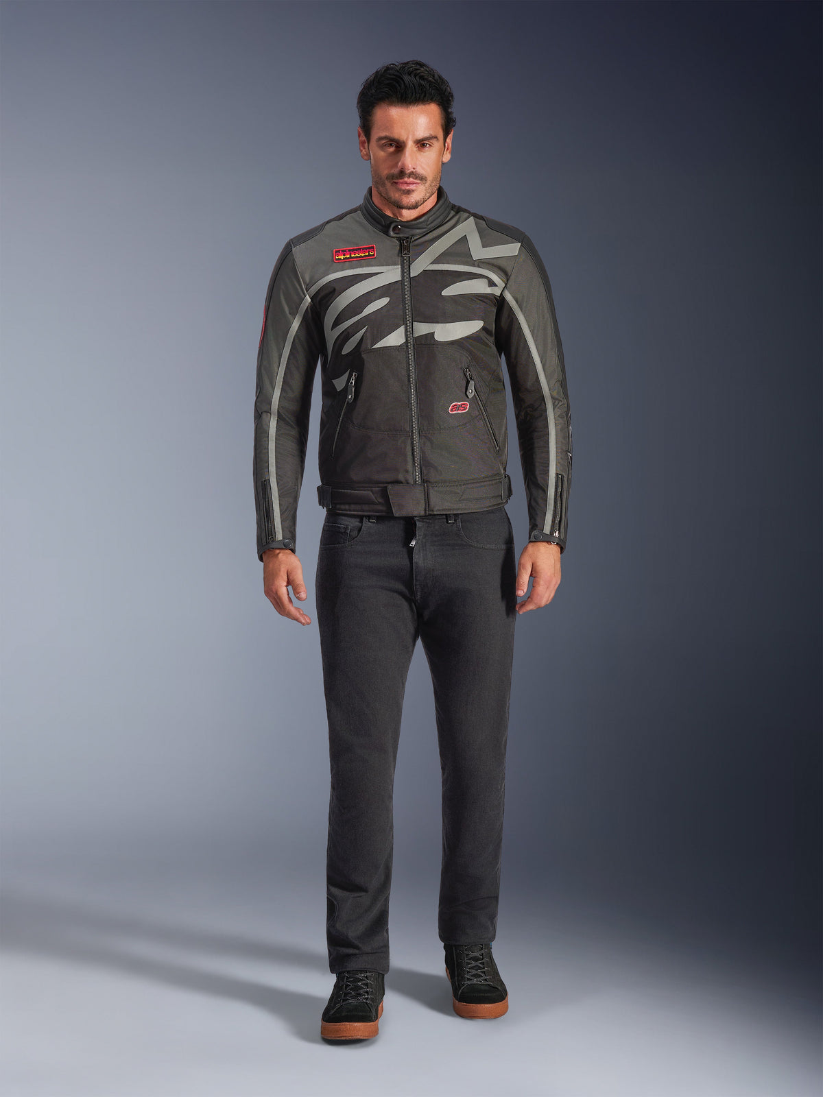 Alpinestars Axton Jacke, Motorradjacke, Schwarz Anthrazit Rot Tangerine, getragen von einem Model mit dunkler Hose, mit umlaufendem grauen Alpinestars-Logo, roten Markenaufnähern und wasserabweisender Textil-Außenschicht für urbane Straßenfahrten