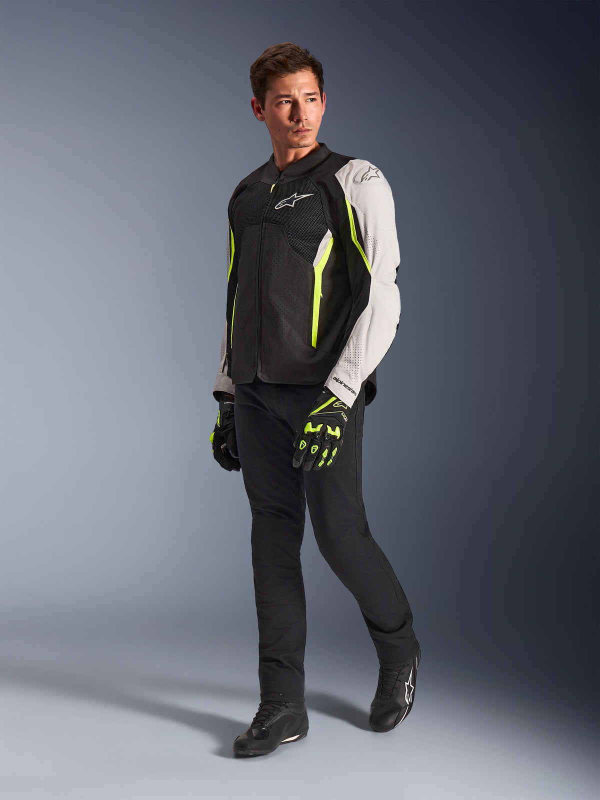 Veste Alpinestars AST V3 Air, veste de moto légère en textile, noir, argent et jaune fluo, portée par un mannequin avec un pantalon noir et des gants assortis, dotée de panneaux en mesh et de perforations au laser pour la conduite sportive par temps chaud.