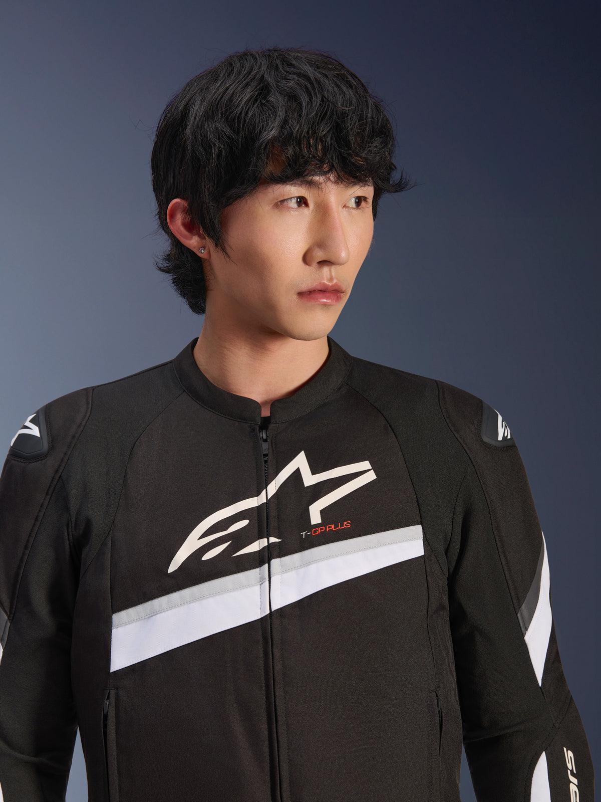 Alpinestars T-GP Plus R V4 Jacket, zwart en wit, textiele motorjas gedragen door een mannelijk model, voorzien van een groot wit sterlogo op de borst, witte diagonale strepen en DFS Lite schouderbeschermers, sportieve motorkleding voor op de weg.