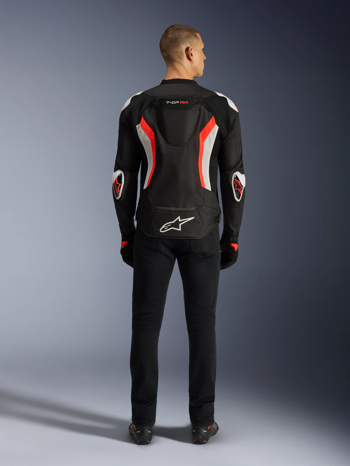 Veste Alpinestars T-GP Air, veste de moto, noir et rouge fluo, vue arrière sur un modèle, dotée d'une bosse aérodynamique, d'accents blancs et rouge fluorescent, logo Alpinestars dans le bas du dos, design à coupe sport pour la conduite sur route.