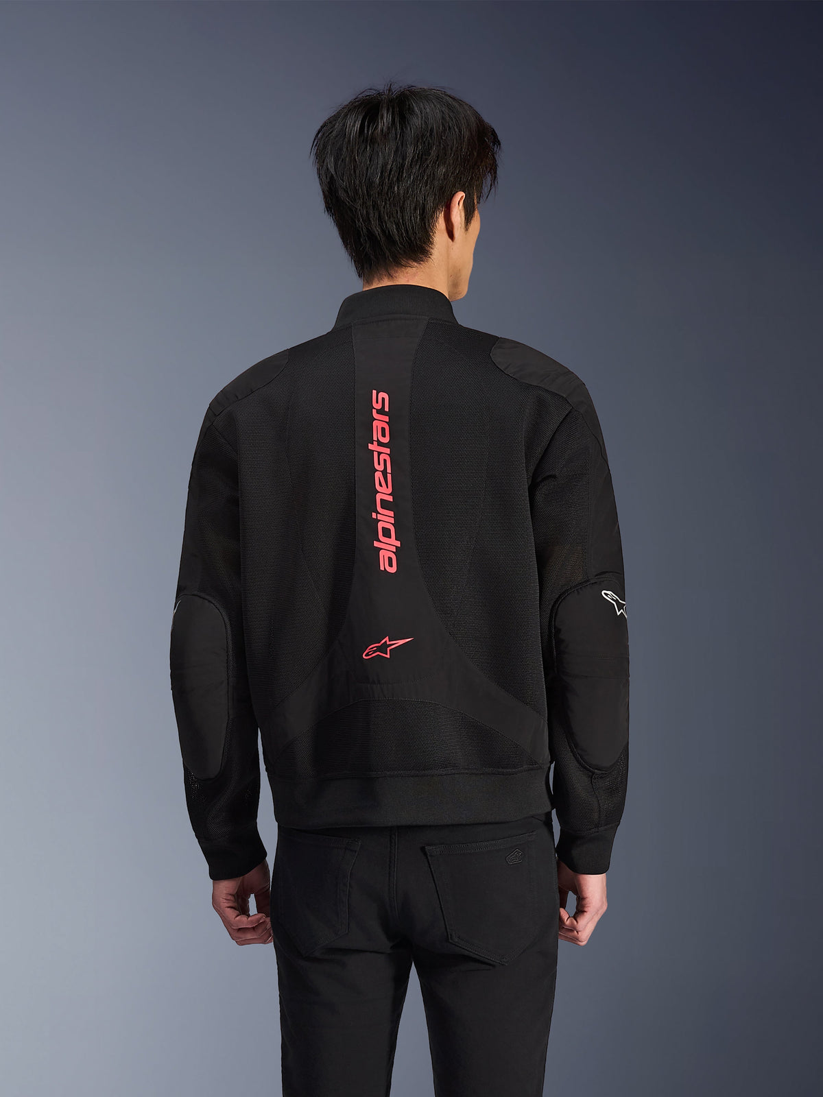 Rückansicht eines Fahrers mit der Alpinestars Flight Air Jacke in Schwarz Leuchtend Rot, Motorradjacke im urbanen Bomber-Stil mit 3D-Mesh-Konstruktion, großes vertikales rotes Alpinestars-Branding und Stern-Logo auf dem Rücken, street-inspirierte technische Ausrüstung