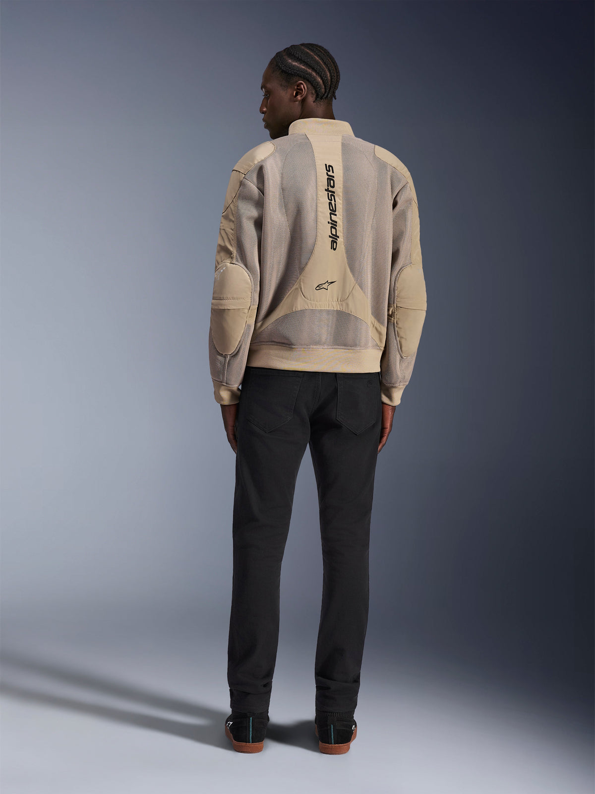 Veste Alpinestars Flight Air, veste de moto urbaine beige, vue arrière montrant les panneaux en maille 3D respirante et le logo vertical, portée avec un pantalon noir pour un look urbain moderne