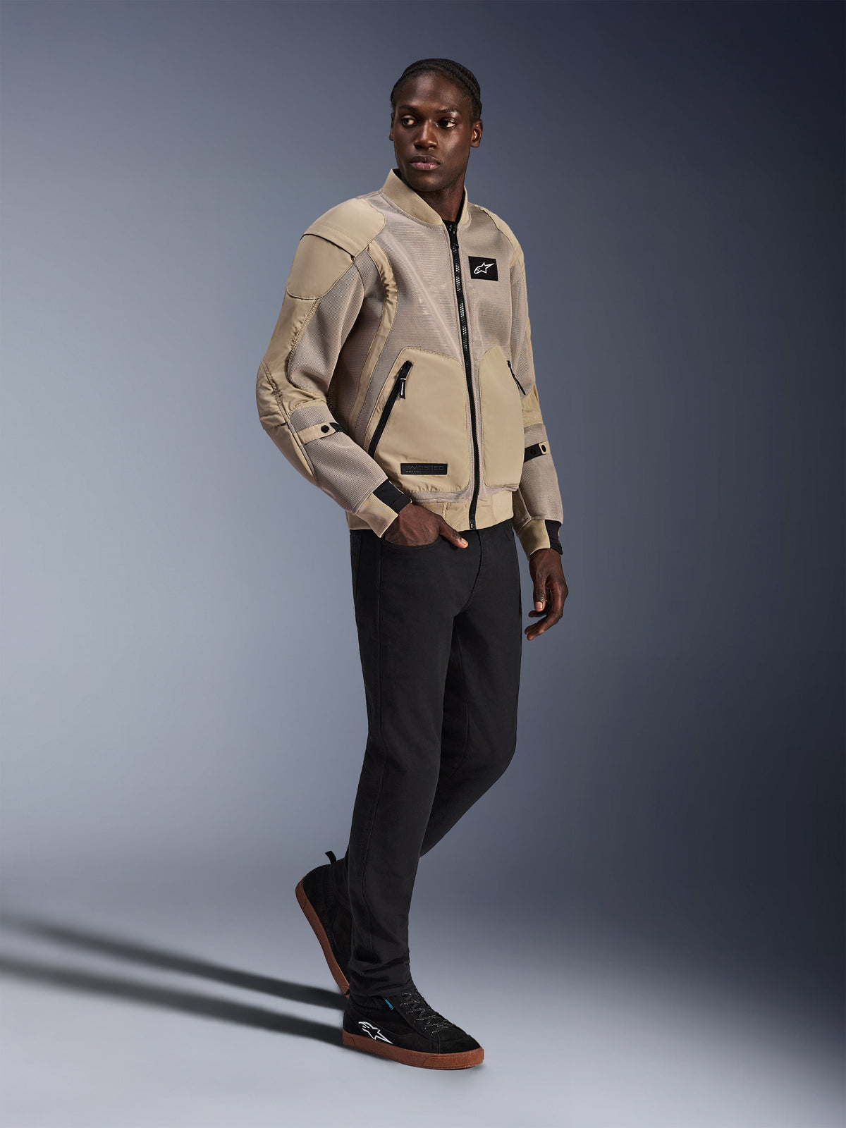 Veste Flight Air Alpinestars, veste de moto urbaine, couleur Aluminum, portée par un mannequin avec un pantalon noir et des baskets noires, dotée de panneaux de ventilation en maille 3D et d'un design de style bomber, style urbain moderne pour la conduite citadine.