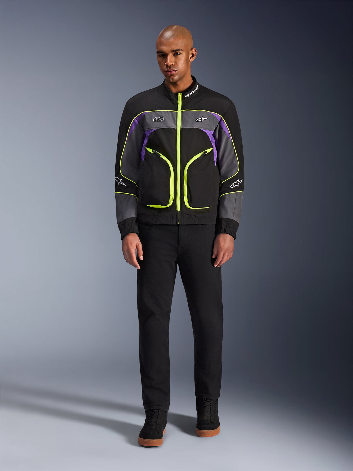 Mannequin homme portant la veste Alpinestars Unite en Black Asphalt Violet, avec une base noire, des empiècements gris et violets et des fermetures éclair et finitions jaune fluo éclatant, associée à un pantalon et des chaussures noirs, veste de moto urbaine minimaliste