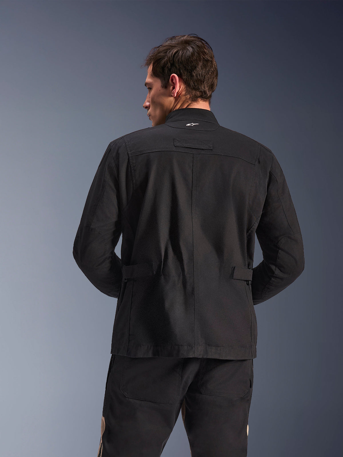 Veste Alpinestars Dice, veste de moto urbaine, noire, vue arrière montrant les épaules plissées et les pattes de réglage à la taille, esthétique de veste de terrain avec petit logo blanc sur le col, équipement textile de protection pour la ville