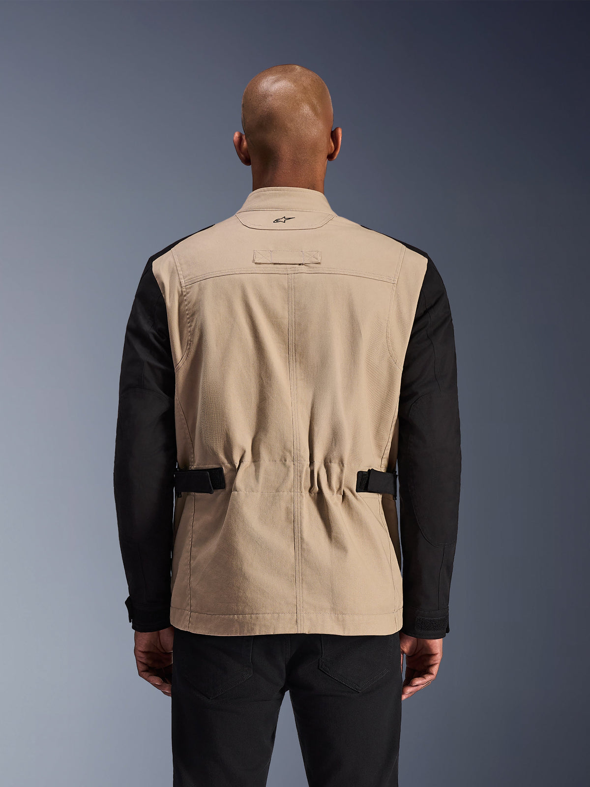 Alpinestars Dice Jacke, urbane Motorradjacke, Aluminium und Schwarz, Rückansicht an einem Modell, plissierte Schultern für Bewegungsfreiheit, verstellbare Taillenriemen, robuste Polycotton-Twill-Konstruktion.