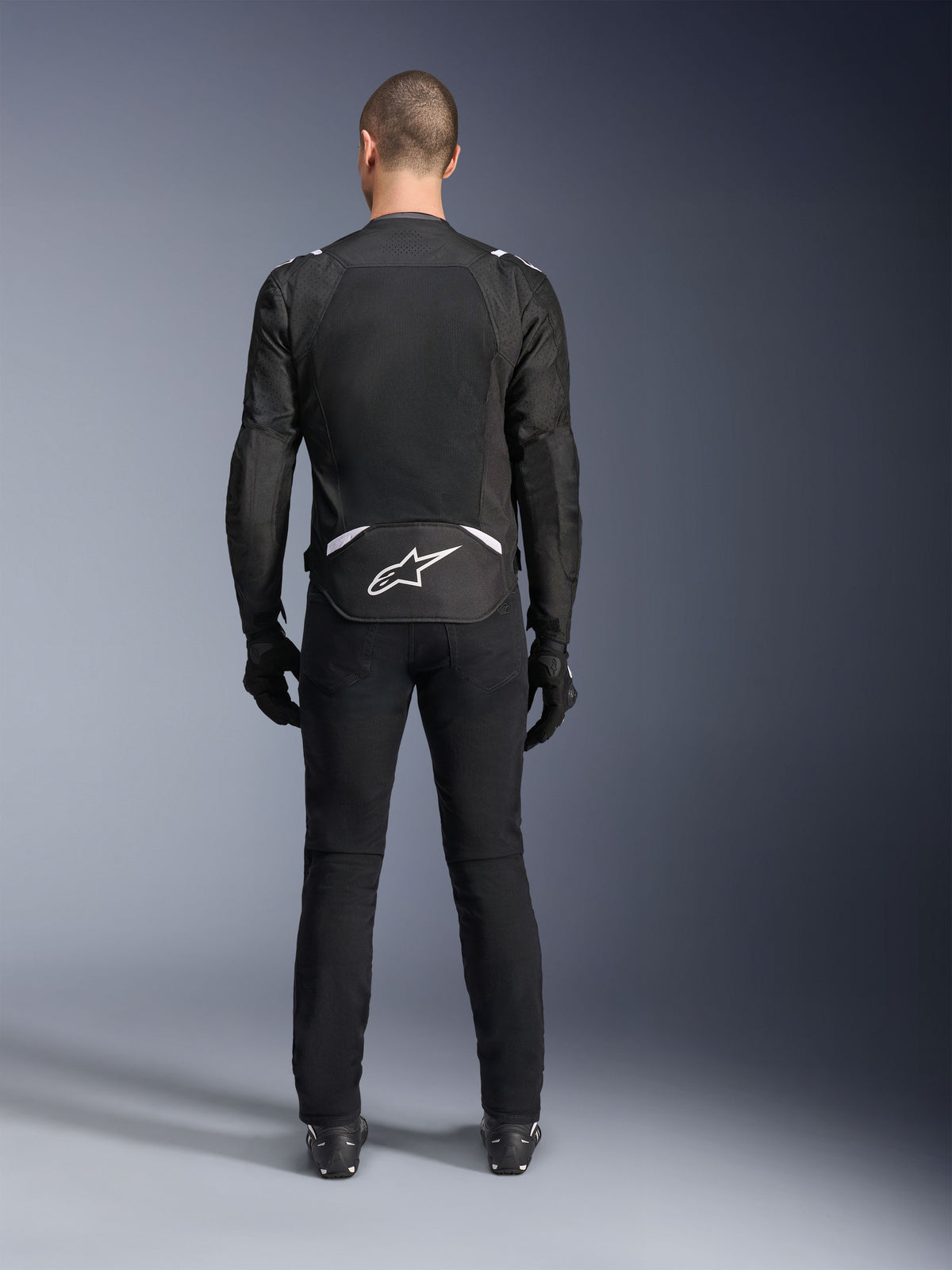 Alpinestars T-Sps Air V2 Jacke, Rückansicht, schwarz-weiße Textil-Motorradjacke, mit großem Mesh-Rückenpanel für maximale Luftzirkulation und weißem Astars-Logo am unteren Rücken, kombiniert mit schwarzer Motorradhose und Handschuhen