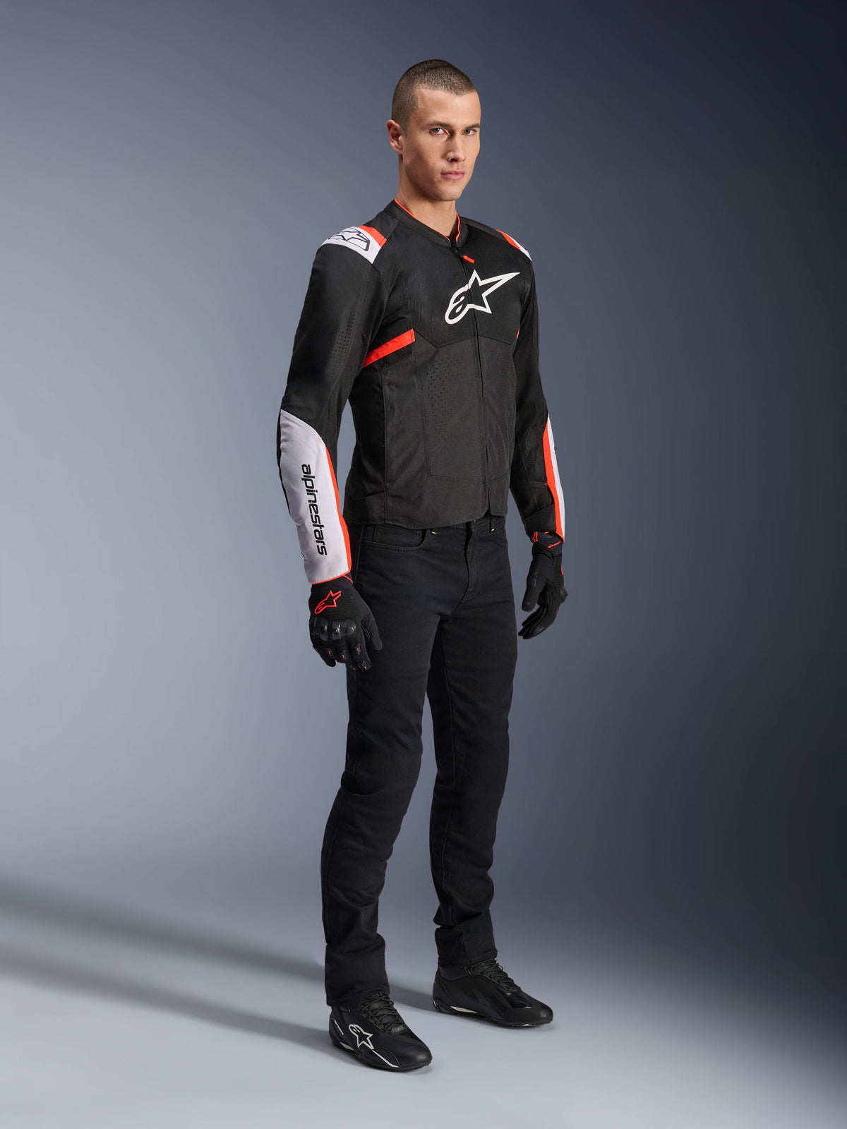 Veste Alpinestars T-Sps Air V2, Noir Blanc Rouge Fluo, portée par un mannequin homme avec un pantalon de moto noir et des gants, veste de moto en textile dotée de grands panneaux en mesh, de sections blanches aux épaules et aux avant-bras, et d'un logo Alpinestars distinctif sur la poitrine.