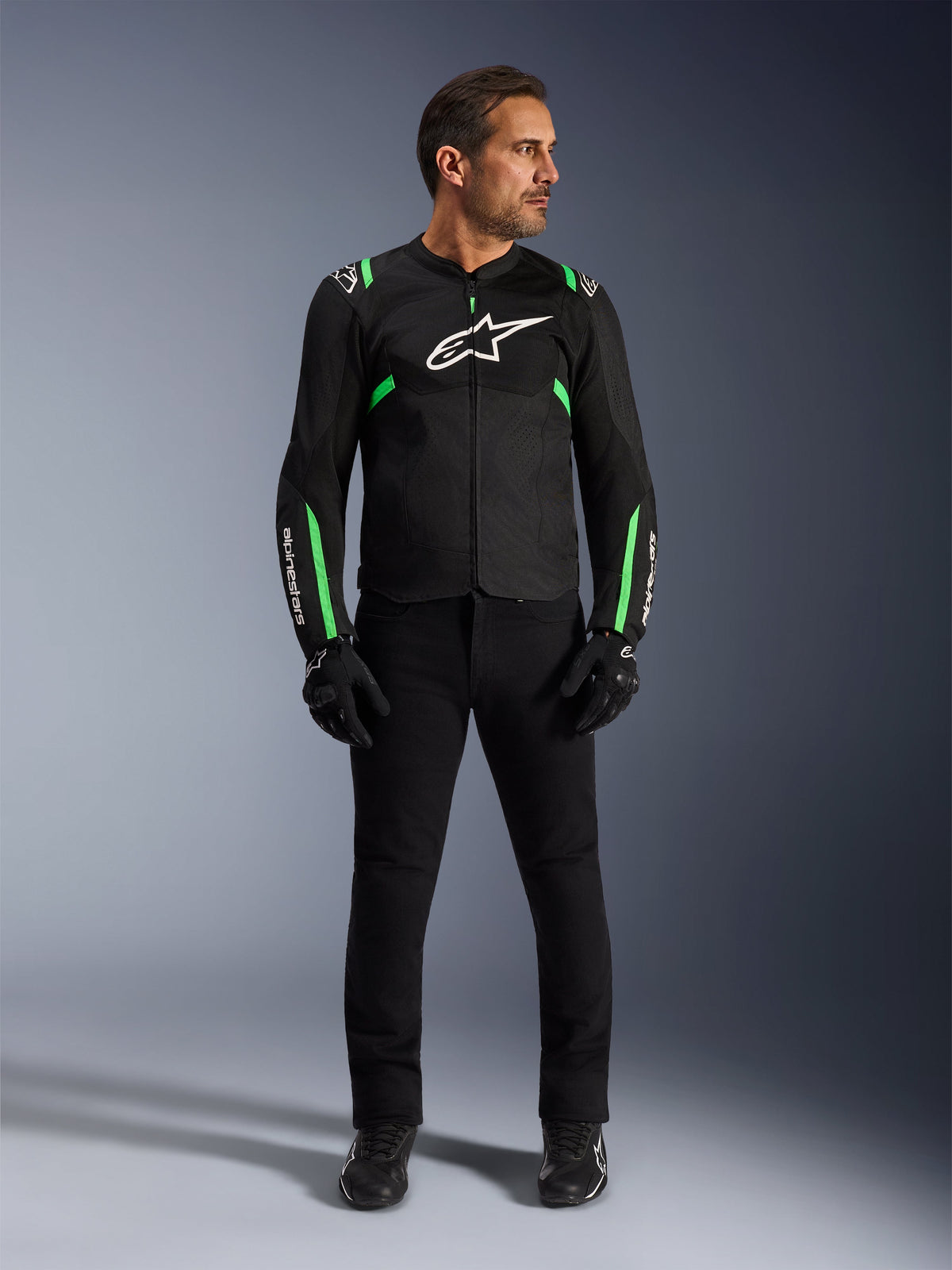 Man wearing the Alpinestars T-SPS Air V2 Jacket in Black Fluo Green, paired with black pants, gloves, and riding shoes, featuring a sport-cut design with white logos and mesh panels for a modern urban riding look.