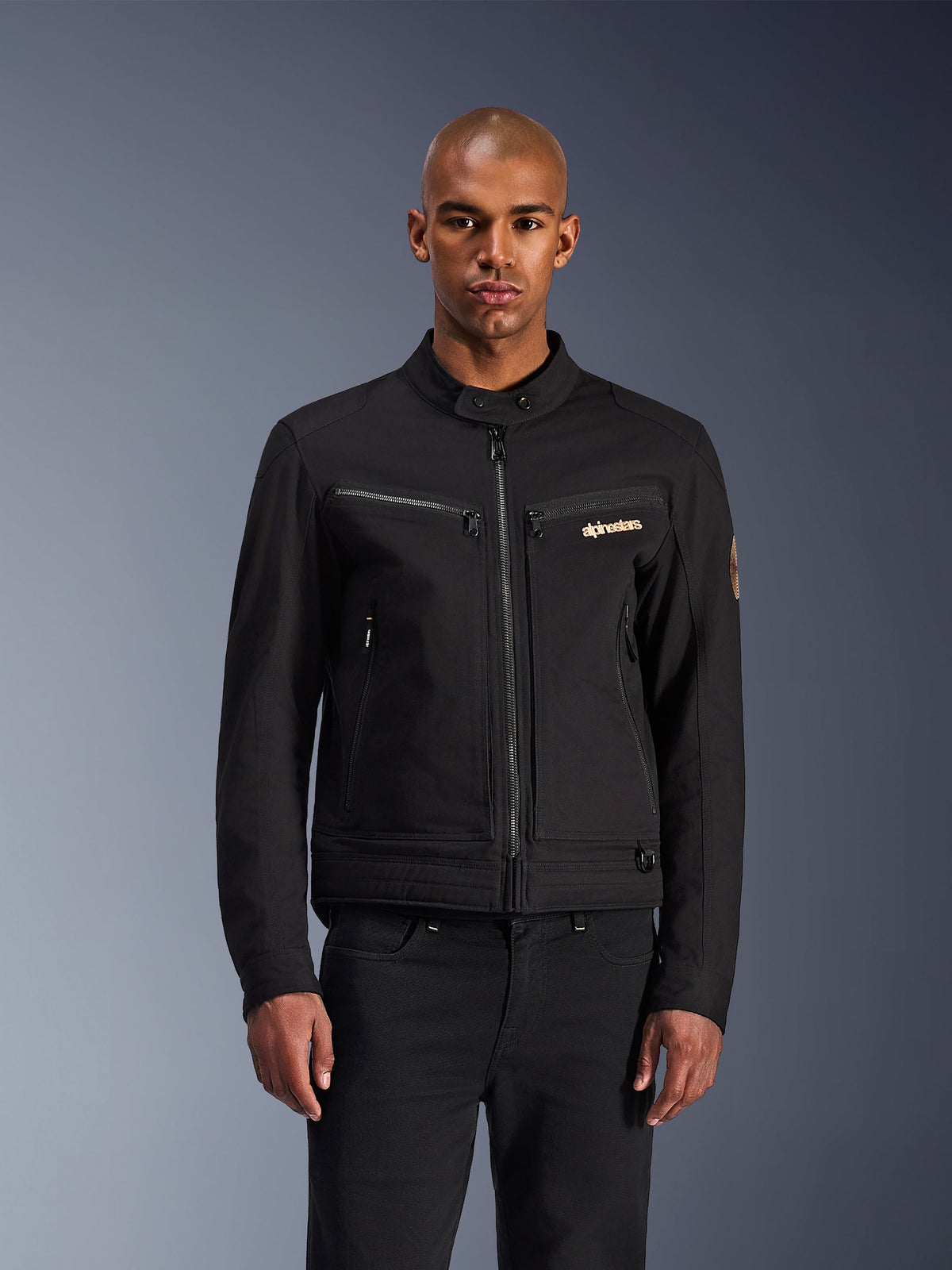 Veste Alpinestars Bruiser, veste de moto urbaine noire, vue de face sur un mannequin, esthétique workwear classique, poches de poitrine zippées, col boutonné et logo Alpinestars, conçue pour les motards urbains