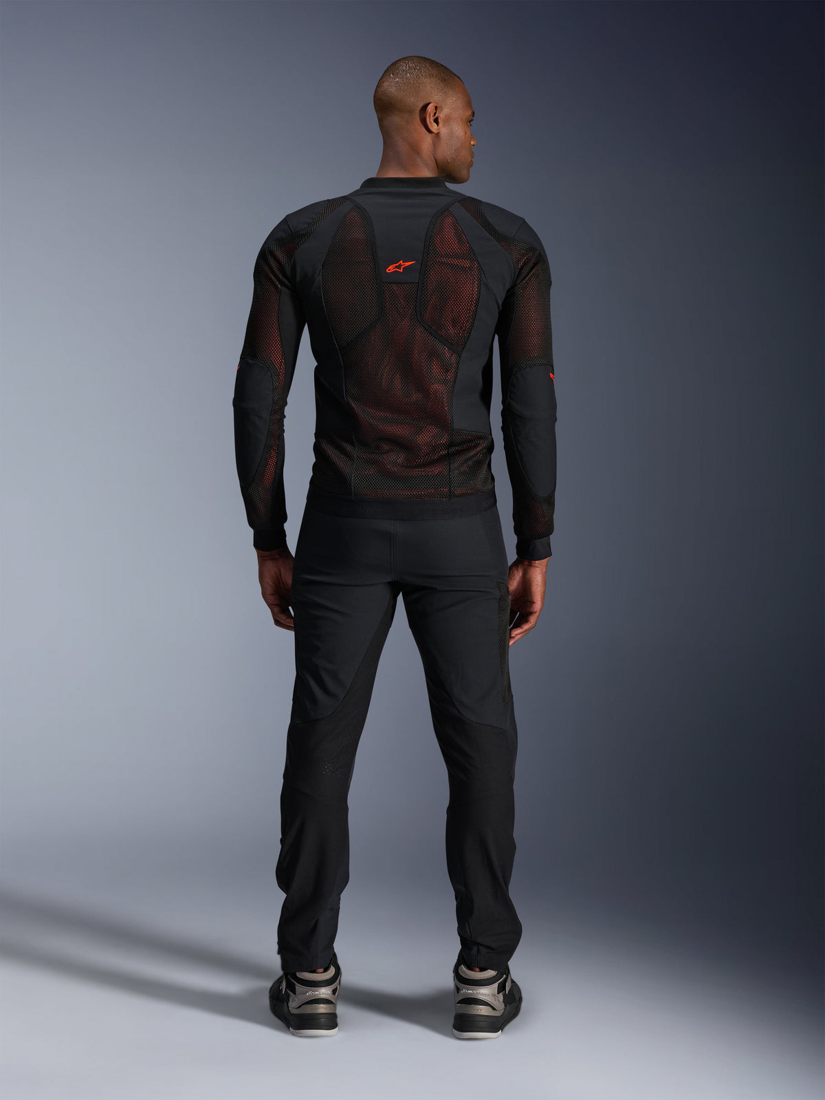 Alpinestars Troop-Air Pro Jas in Black Red Fluo, achteraanzicht op model, technische mesh jas met protectie en ademende panelen, rood logo op de bovenrug, gedragen met zwarte broek en sneakers, urban motorkleding