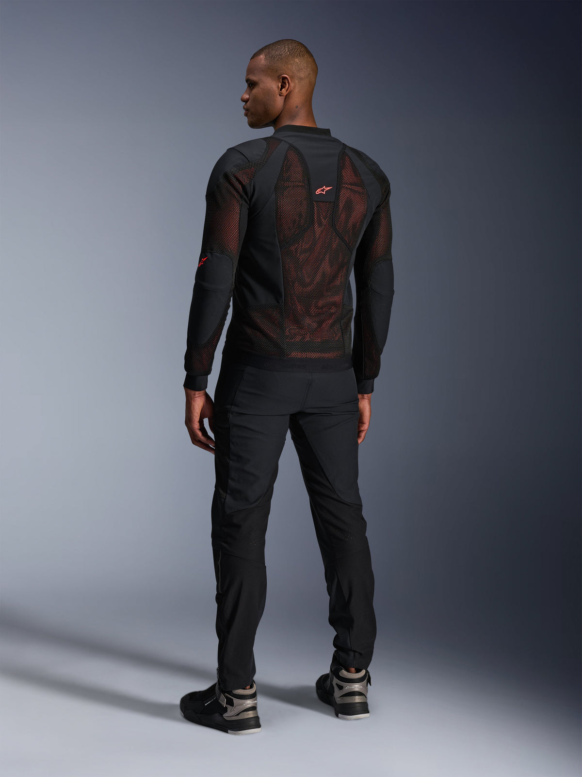 Alpinestars Troop-Air Pro Jacket in Black Red Fluo, achteraanzicht op een model, voorzien van een groot 2D tech mesh achterpaneel met zichtbare rode binnenkant, gecombineerd met een zwarte technische motorbroek en zwart-grijze laarzen, modern urban motorjasontwerp met protectie.