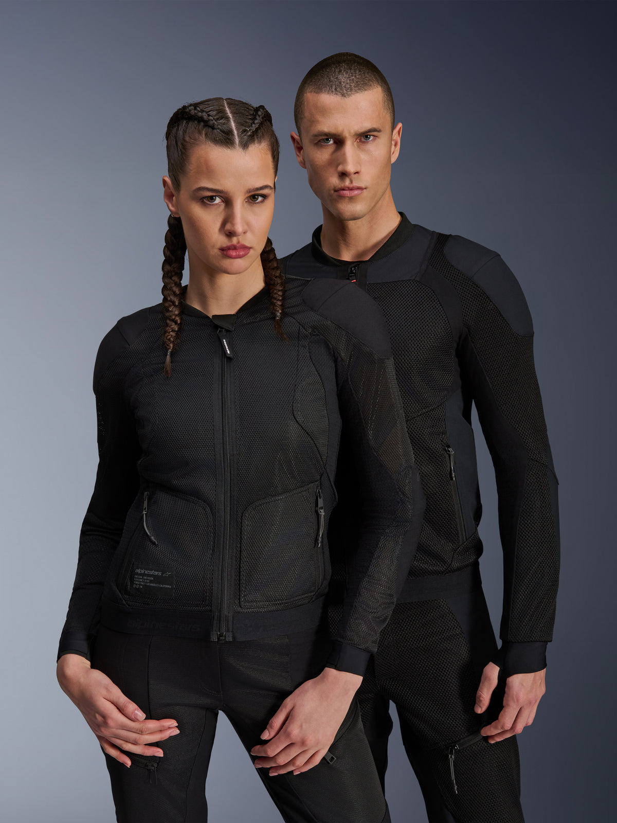 Homme et femme portant les vestes Alpinestars Troop-Air et Stella Troop-Air, vestes de moto techniques en maille noire, avec structure en maille technique 2D pour la ventilation et panneaux renforcés, tenue de conduite urbaine contemporaine