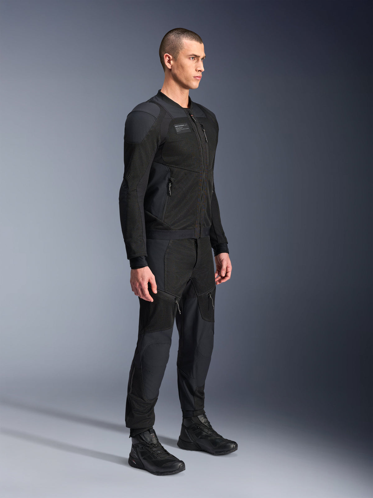 Alpinestars Troop-Air Pro Jacke, technische gepanzerte Air-Jacke, Schwarz, getragen von einem Model mit passender schwarzer Motorradhose und Stiefeln, mit fortschrittlicher 2D-Tech-Mesh-Struktur und atmungsaktiven Belüftungspanelen, moderne urbane Motorradbekleidung.